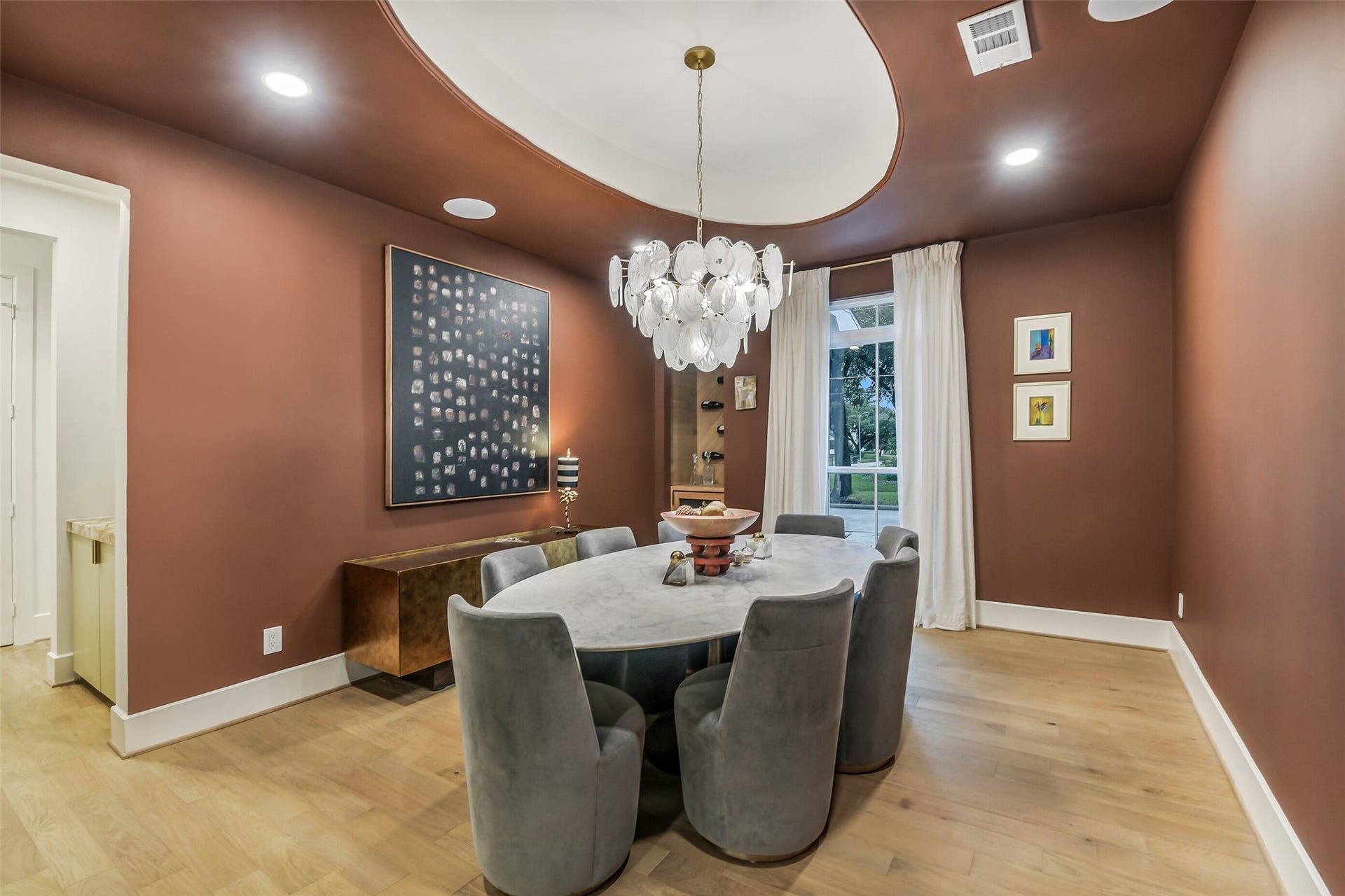 9411 Millbury Drive, Houston, TX 77096 A rich, moody color palette sets the tone in this elegant dining room, anchored by a round table with plush swivel chairs beneath a sculptural bubble chandelier. A domed ceiling detail and curated artwork add a refined, sophisticated touch.