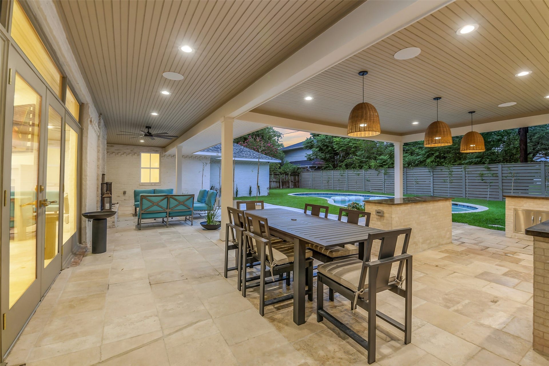 9411 Millbury Drive, Houston, TX 77096 A resort-style covered patio featuring a full outdoor kitchen with bar seating, a wood-look ceiling with recessed lighting, and a dining area overlooking the pool perfect for year-round entertaining and al fresco dining.