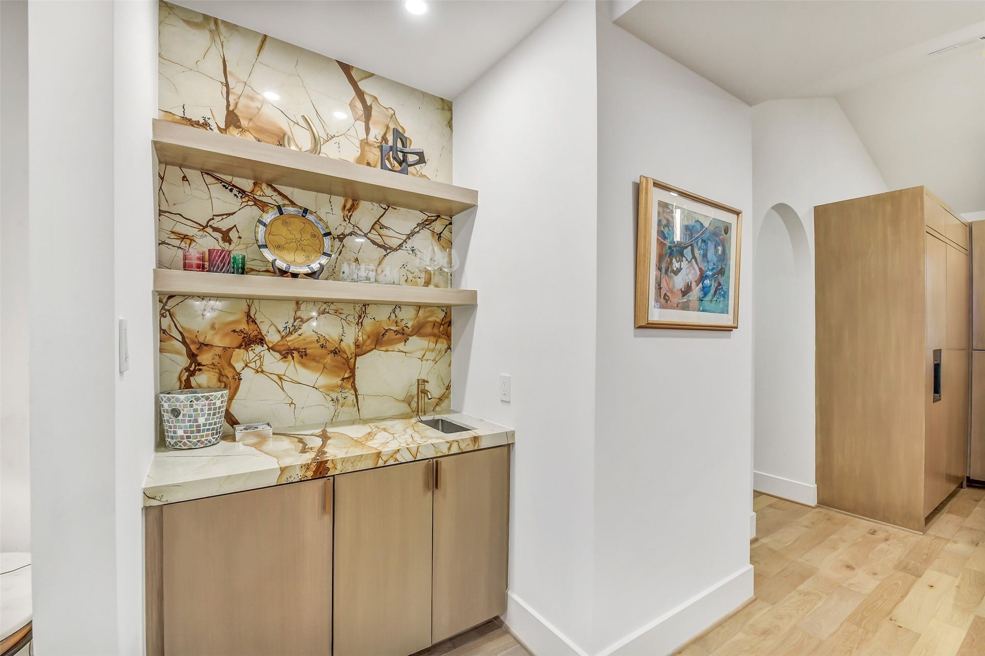 9411 Millbury Drive, Houston, TX 77096 A stylish wet bar tucked just off the main living space, featuring dramatic natural stone backsplash, open shelving, and warm wood cabinetry perfect for storing glassware and entertaining essentials.