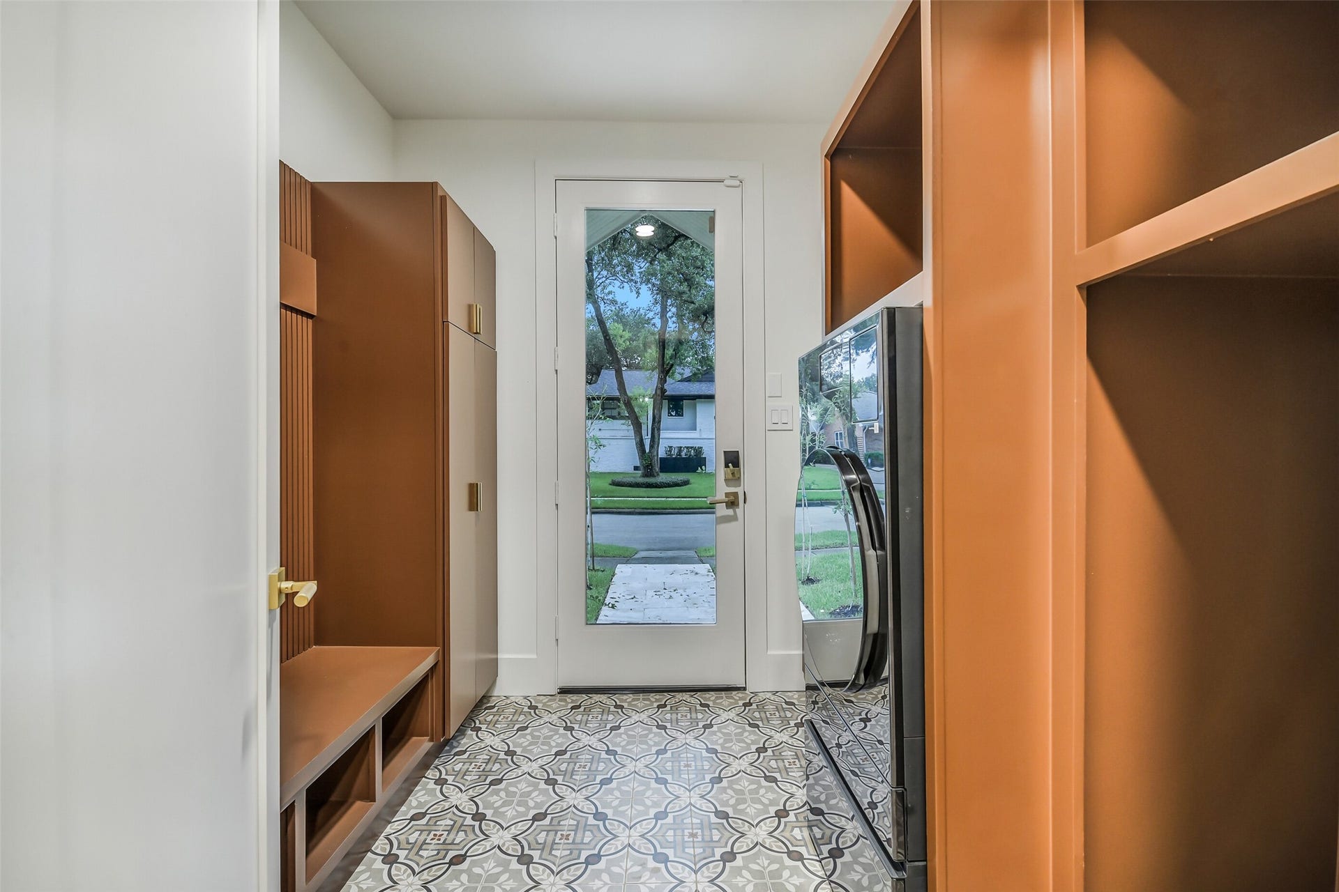 9411 Millbury Drive, Houston, TX 77096 A stylish mudroom finished with patterned tile flooring and rich, custom cabinetry featuring fluted detailing and brass hardware. Built-in storage and a bench offer a functional drop zone, while a sleek all-in-one washer/dryer combo adds everyday convenience just steps from the back door.