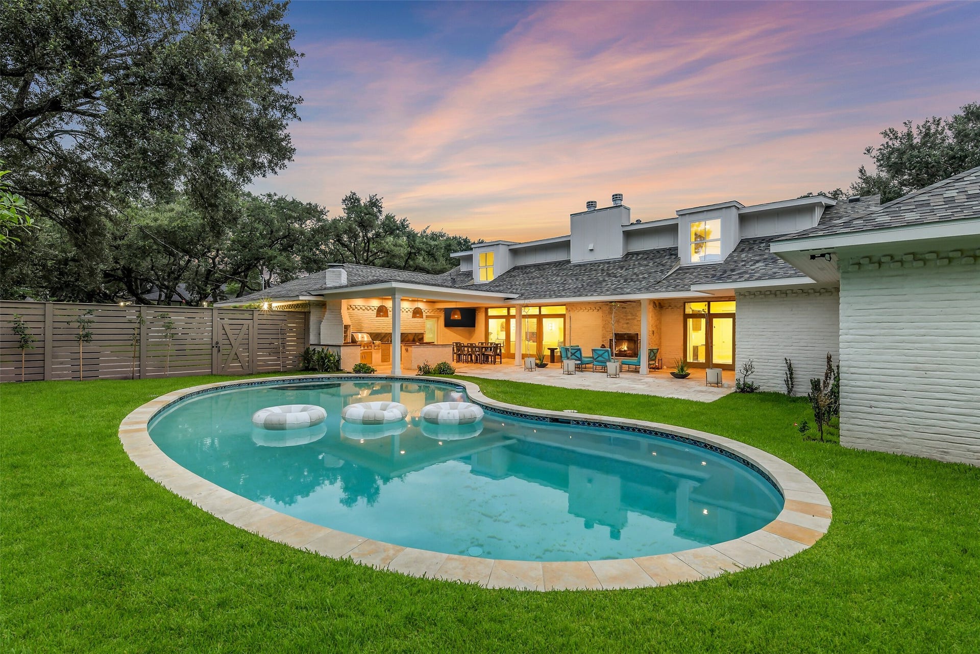 9411 Millbury Drive, Houston, TX 77096 A freeform pool anchors this beautifully landscaped backyard, surrounded by lush green lawn and mature trees for privacy. The adjoining covered patio adds an outdoor kitchen and fireplace, creating a seamless indoor-outdoor flow an entertainer's paradise from morning through dusk.