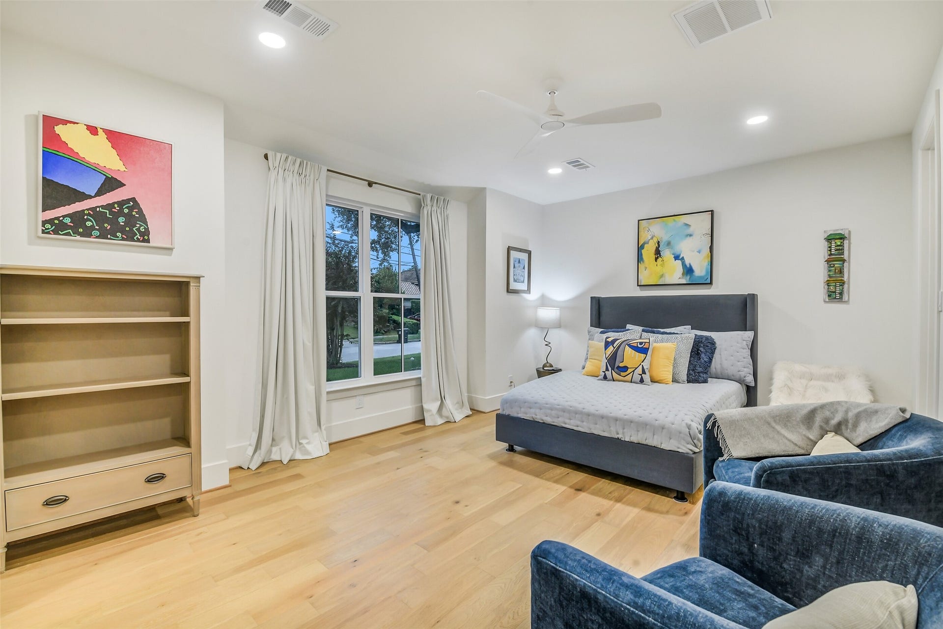 9411 Millbury Drive, Houston, TX 77096 A bright, generously sized secondary bedroom with large windows overlooking the front yard, a ceiling fan, and plenty of room for both a bed and a cozy sitting area. Neutral tones and light wood flooring keep the space airy and adaptable.