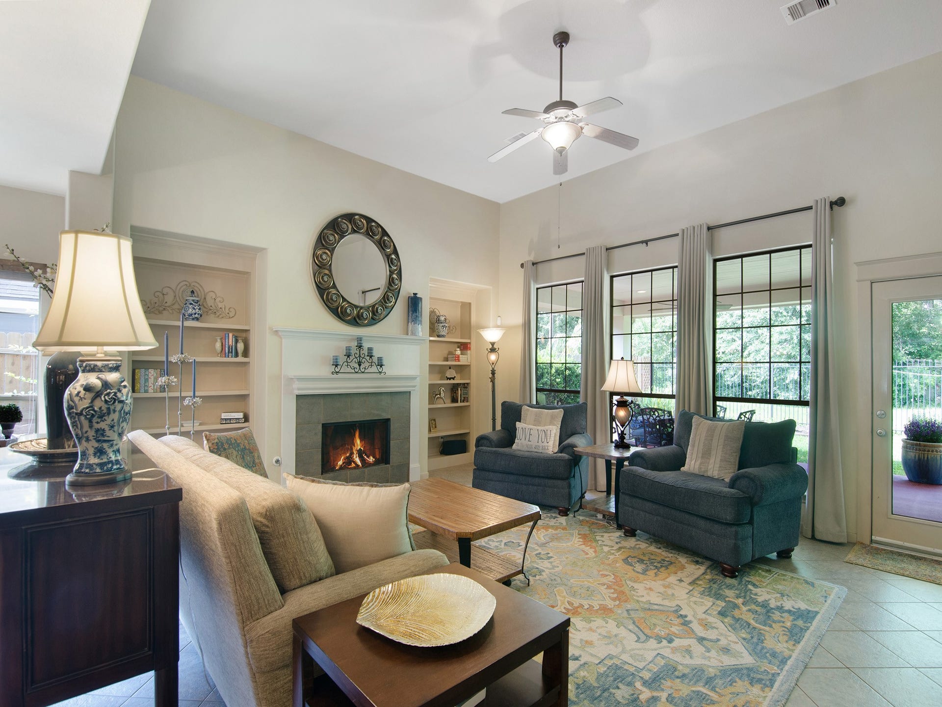 Light-filled family room with soaring ceilings, built-in shelving, tile-surround fireplace overlooking backyard greenspace.