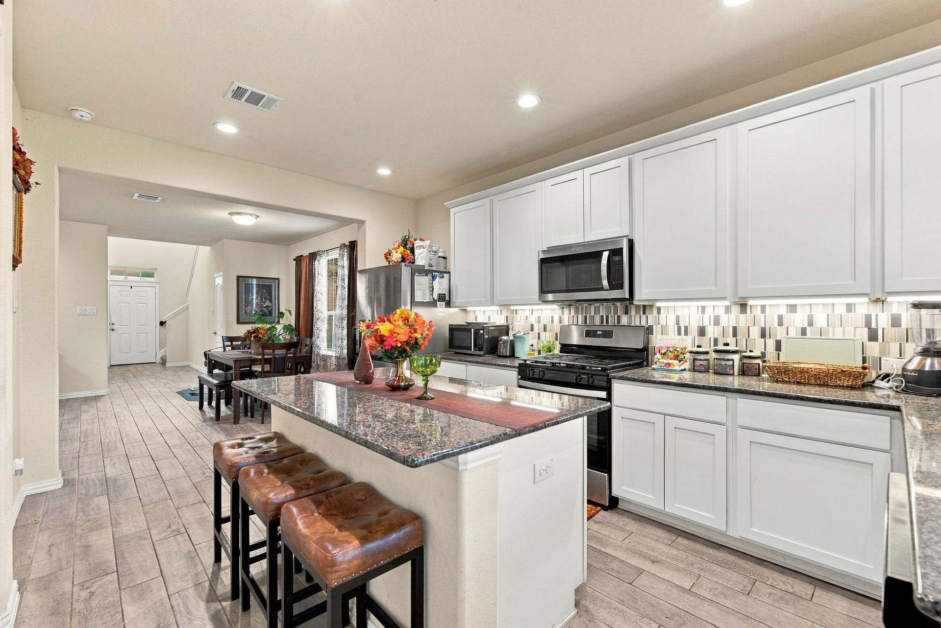 13202 Dancing Reed Drive, Texas City, TX 77568 Beautiful and modern kitchen with sleek white cabinetry, granite countertops, and a stylish tile backsplash. An inviting breakfast bar with seating opens to a cozy dining area, perfect for family gatherings.