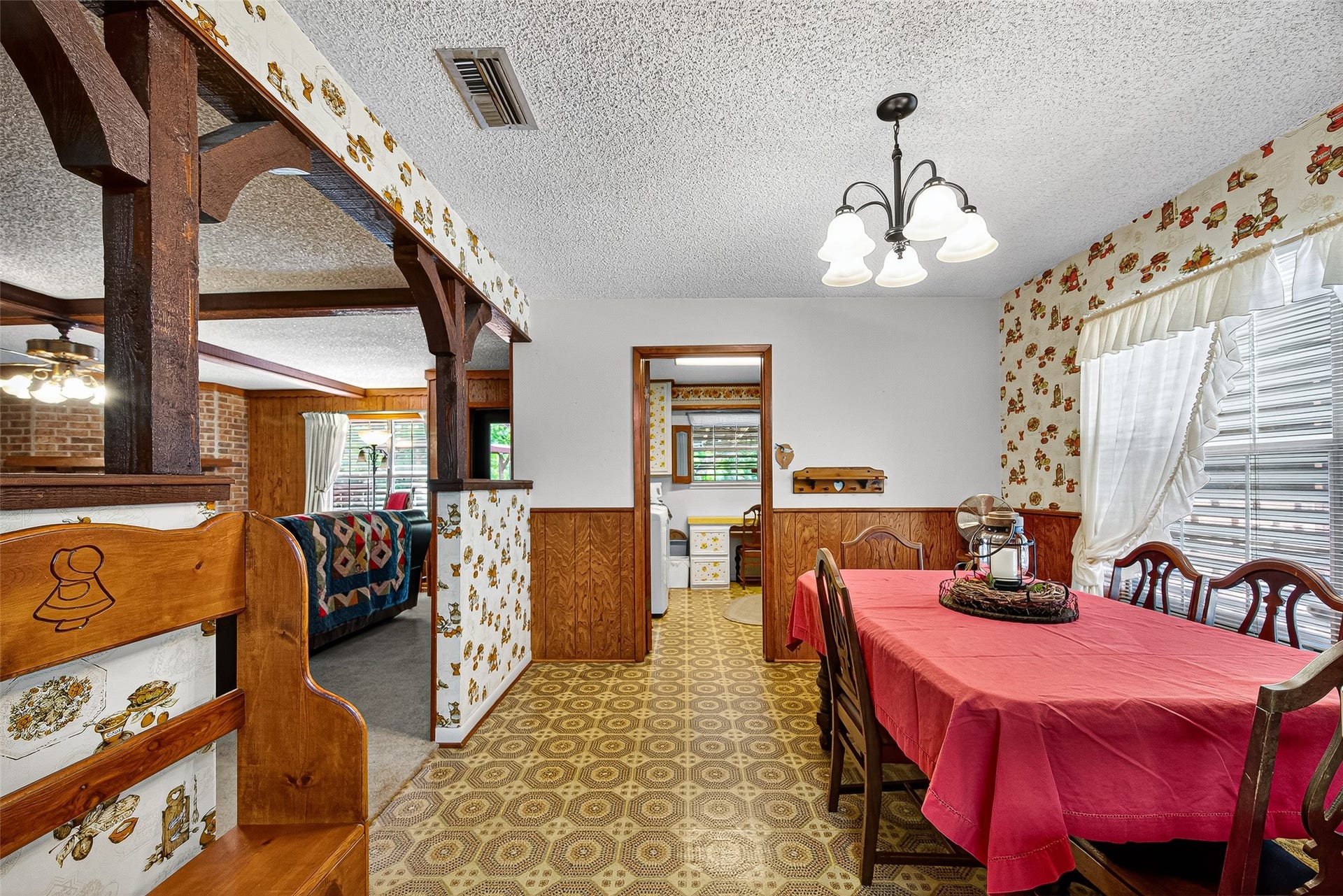 12021 7th 1/2 Street, Santa Fe, TX 77510 A chandelier adds charm, and large windows with sheer curtains bring in natural light. The space opens into a carpeted living room with exposed brick and wooden beams for a rustic feel.