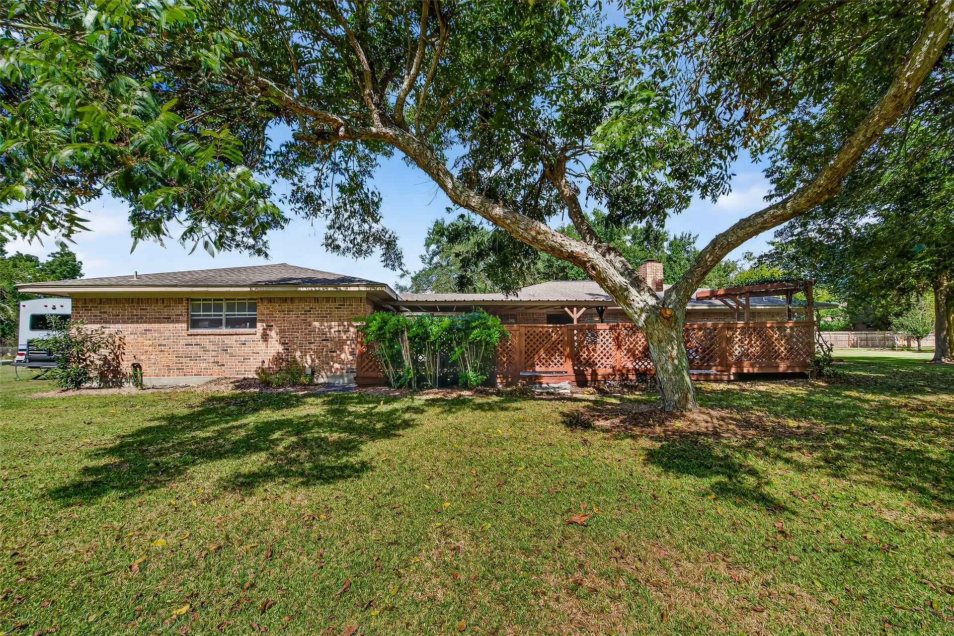 12021 7th 1/2 Street, Santa Fe, TX 77510 Charming brick home with a spacious backyard featuring lush grass and mature trees. A wooden patio area provides shade and outdoor living space, perfect for relaxation and entertaining.