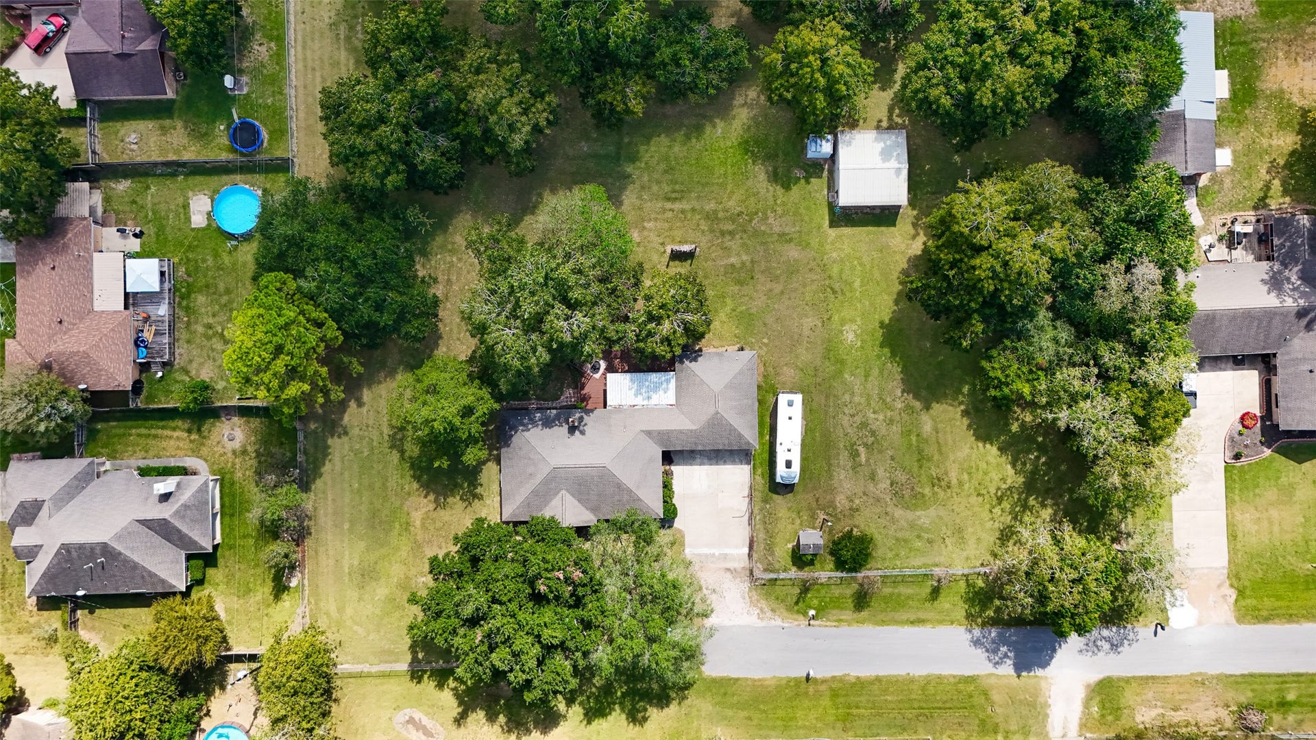 12021 7th 1/2 Street, Santa Fe, TX 77510 This aerial photo shows a spacious property with a large, well-maintained yard surrounded by mature trees. The house has a sizable driveway and is situated in a quiet, residential neighborhood. There are neighboring homes with pools visible, indicating a family-friendly area.