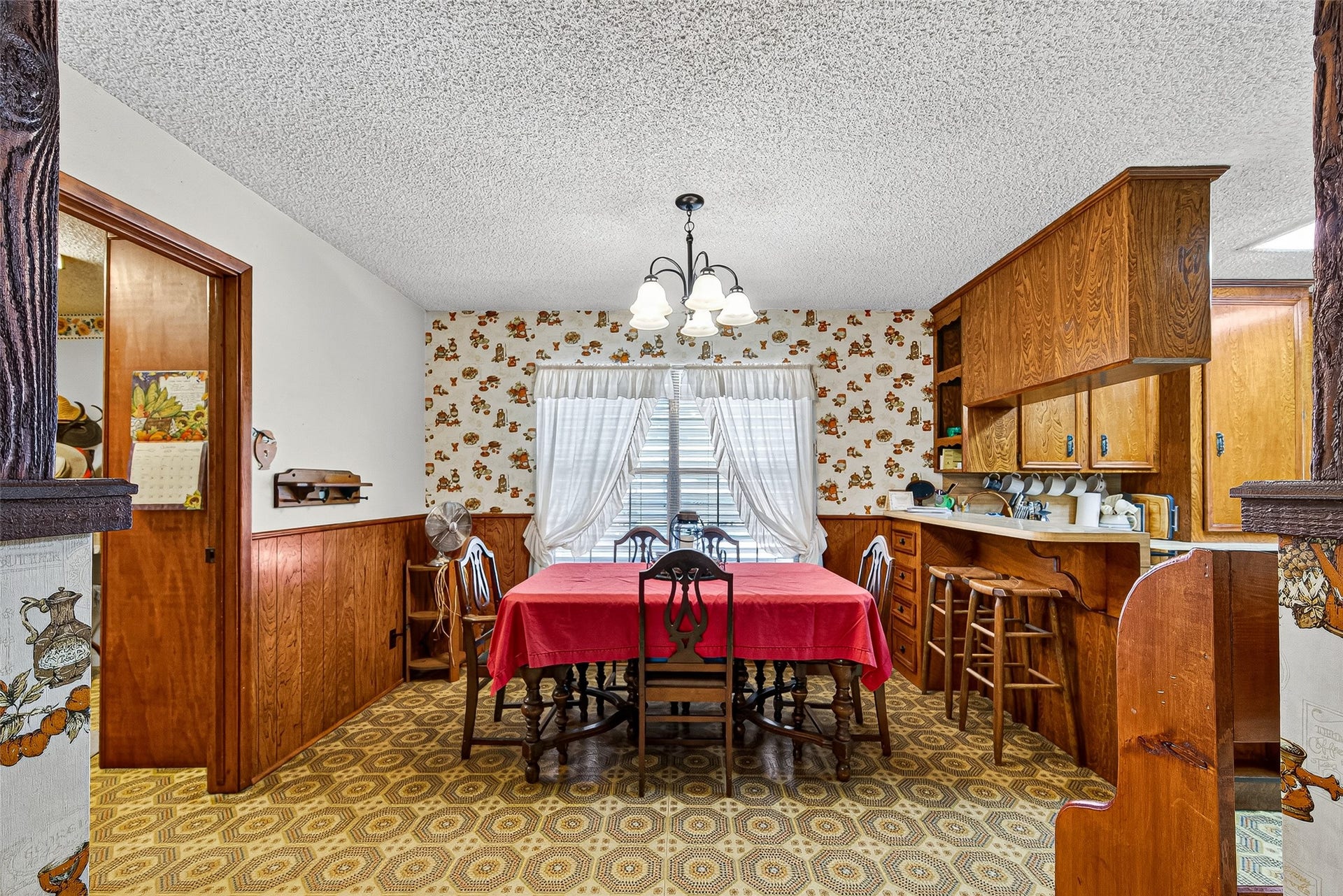 12021 7th 1/2 Street, Santa Fe, TX 77510 This cozy dining area features vintage charm with floral wallpaper and wood paneling A built-in kitchen nook with ample storage and counter space. A window with drapes allows natural light to brighten the space.