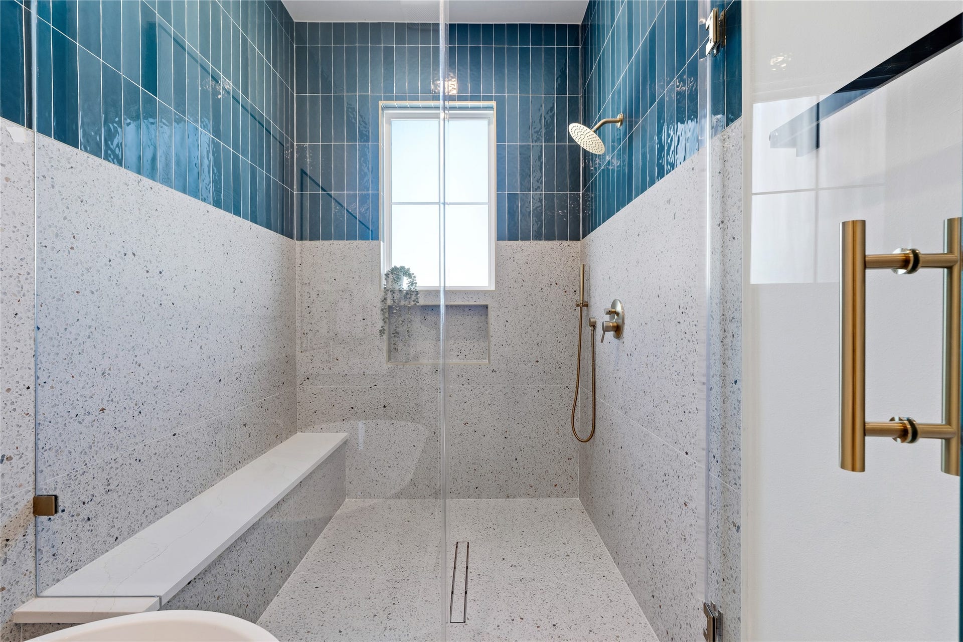 4610 Gunter Street, Houston, TX 77020 A frameless glass partition defines the spacious walk-in shower, which includes a built-in bench and linear floor drain. The architecture utilizes a central window to flood the tiled space with natural light.