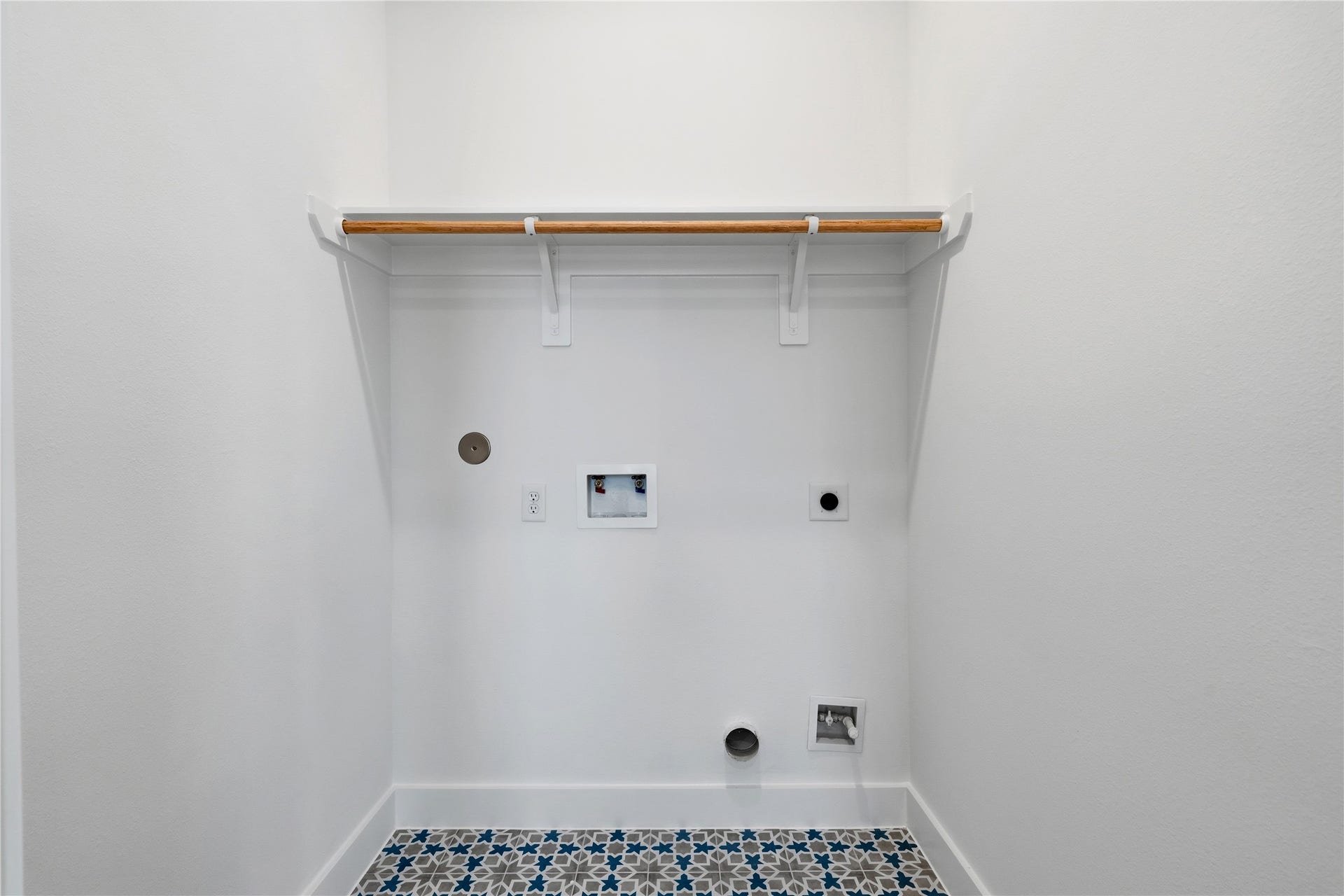 4610 Gunter Street, Houston, TX 77020 A dedicated laundry alcove featuring patterned Mediterranean-style floor tiles and a natural wood hanging rod. The minimalist white environment includes integrated plumbing and electrical connections for a streamlined look.
