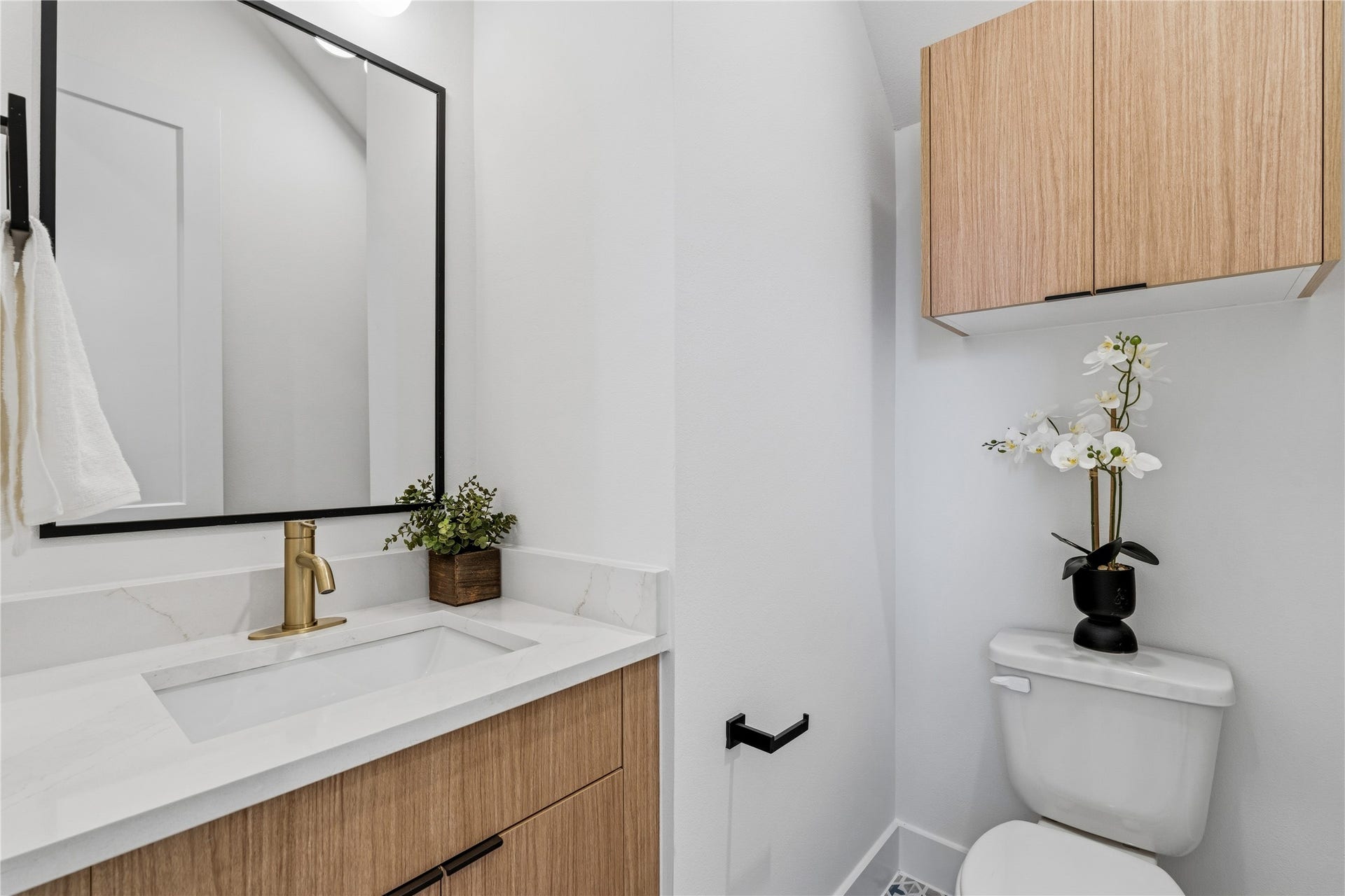 4610 Gunter Street, Houston, TX 77020 A sophisticated bath featuring a light wood vanity topped with white stone and a brushed gold faucet. Black-framed accents and patterned tiling add a modern, high-contrast touch to the compact space.