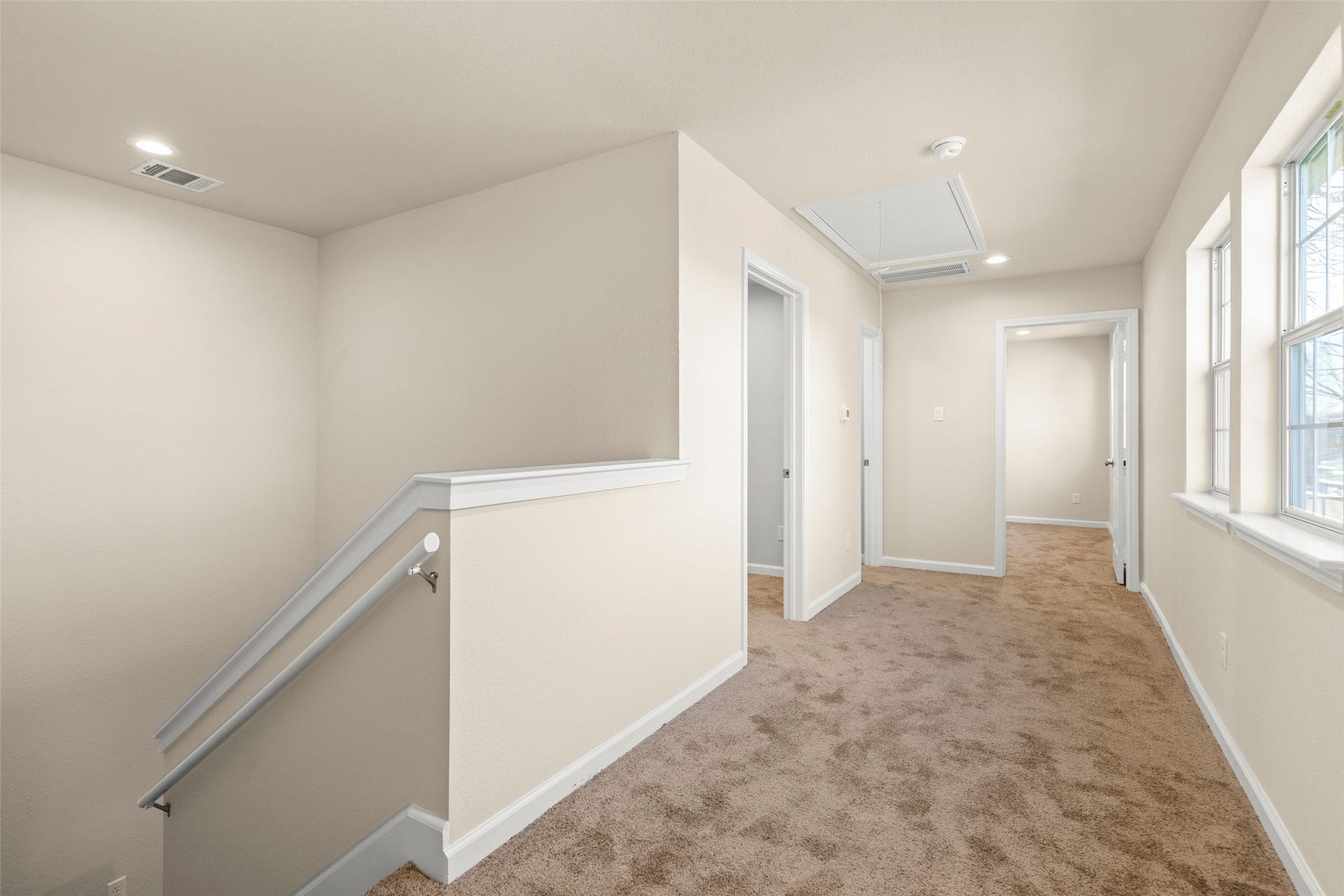 This photo shows a two-story modern home with a light exterior and a small upper balcony. It features a gated driveway and a fenced yard, providing privacy and security. The property is flanked by similar homes and surrounded by trees, offering a cozy neighborhood feel.