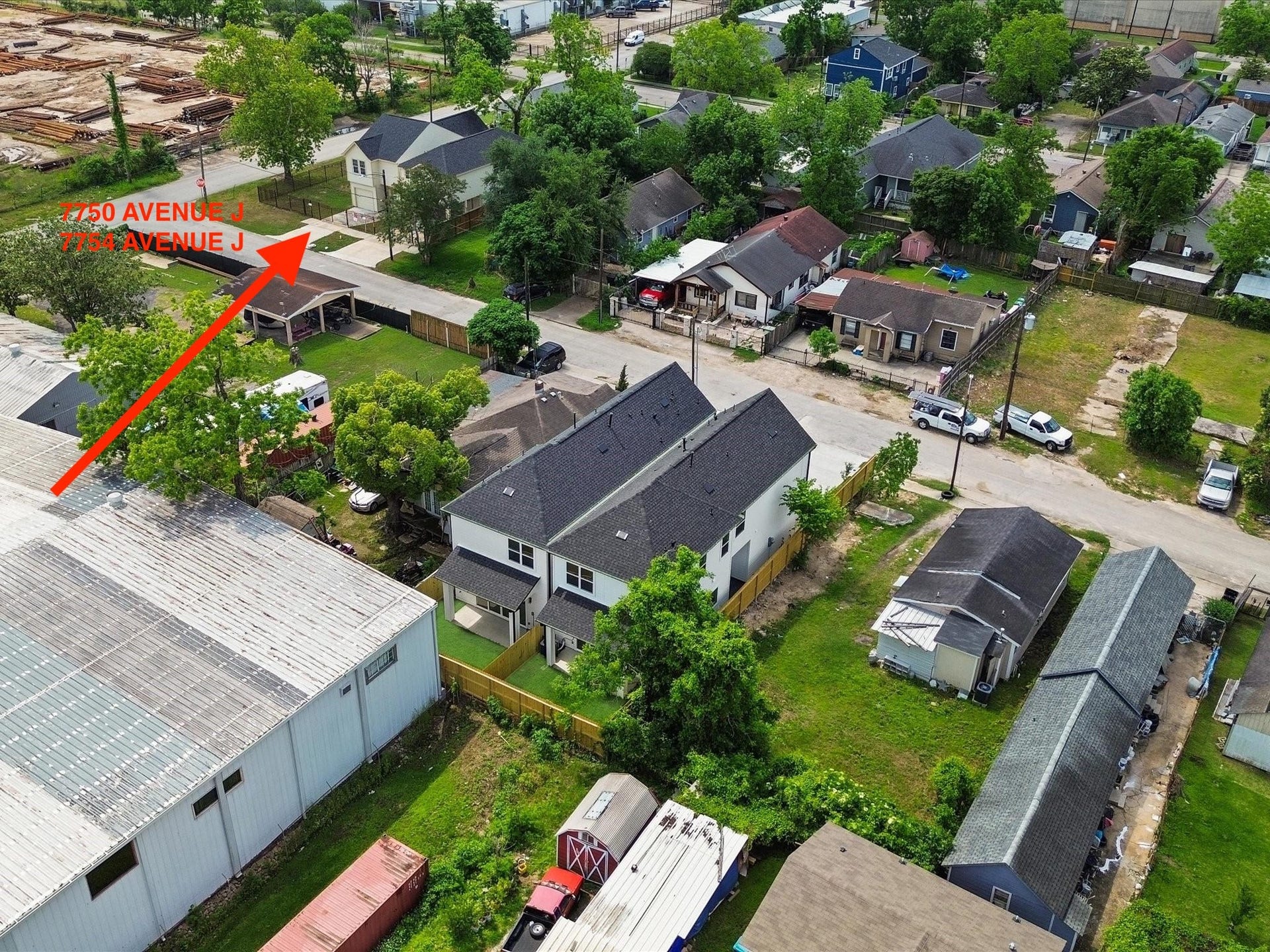 This photo shows a covered carport area attached to a house with beige siding. It opens onto a concrete driveway, enclosed by a wooden fence and a metal gate. Theres some grass and a few trees visible, offering a sense of privacy.