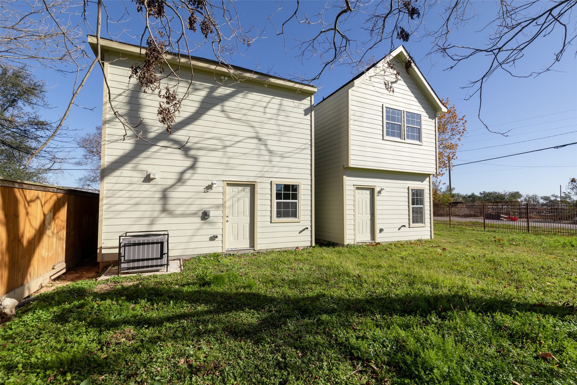 This room features neutral walls, carpeted flooring, and a ceiling fan with lights. It has large windows providing natural light and a view of the outdoors. A white door leads to another area of the home.