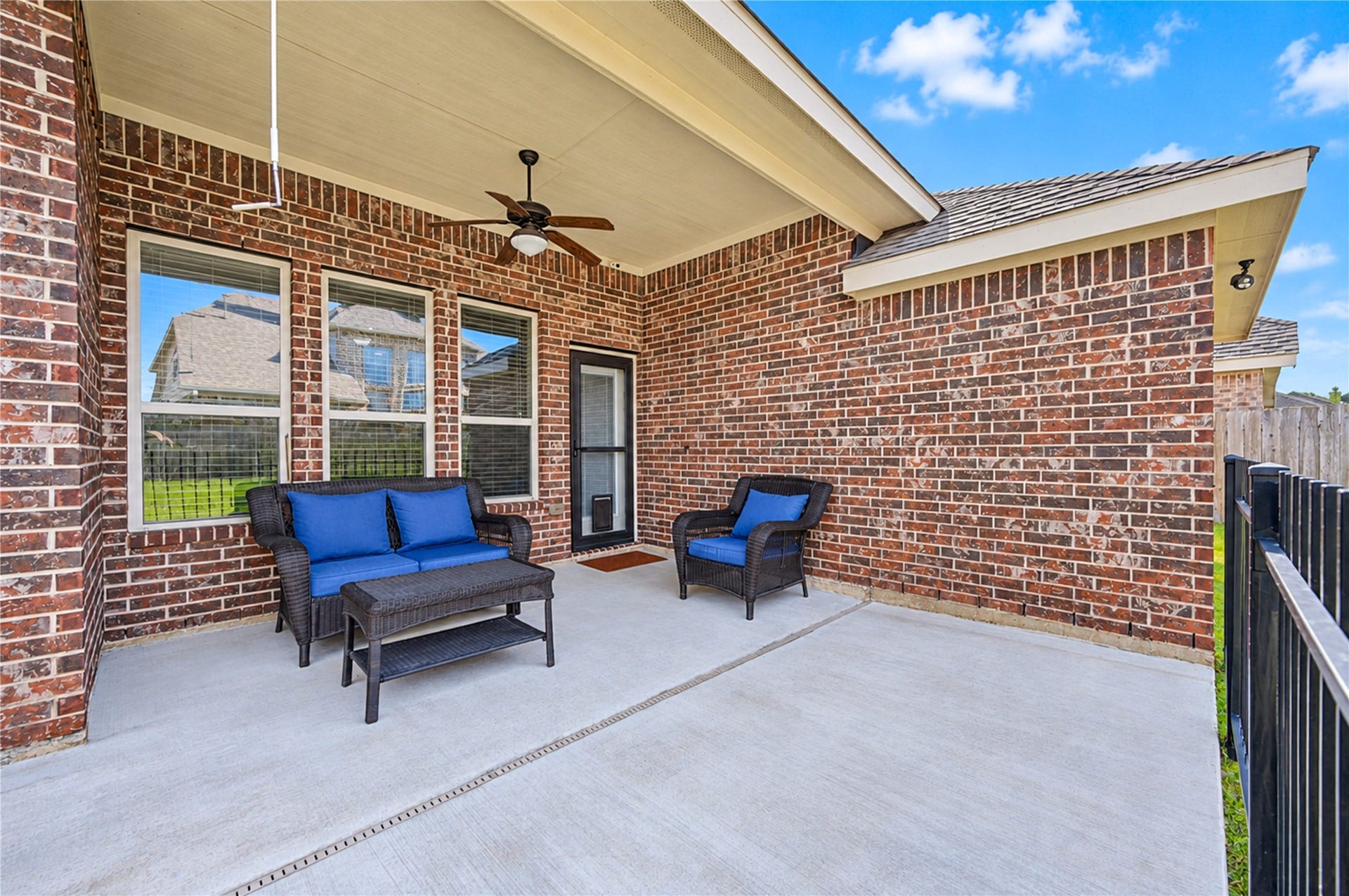 16719 Cactus Blossom Trail, Cypress, TX 77433 A concrete covered patio with a ceiling fan sits against the home's brick exterior.