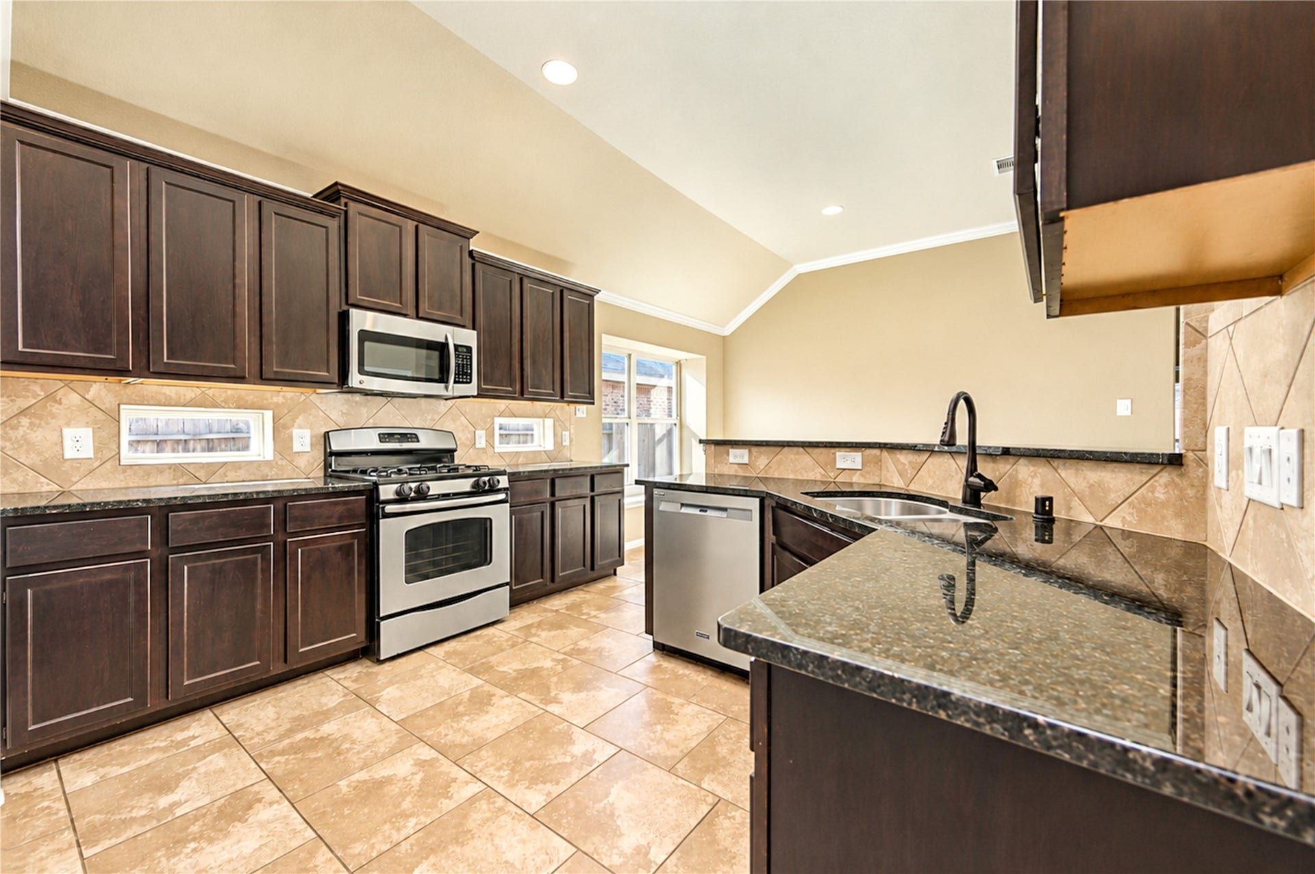 16719 Cactus Blossom Trail, Cypress, TX 77433 Warm cabinetry, a tile backsplash and a vaulted ceiling give the kitchen an inviting, well-organized layout.