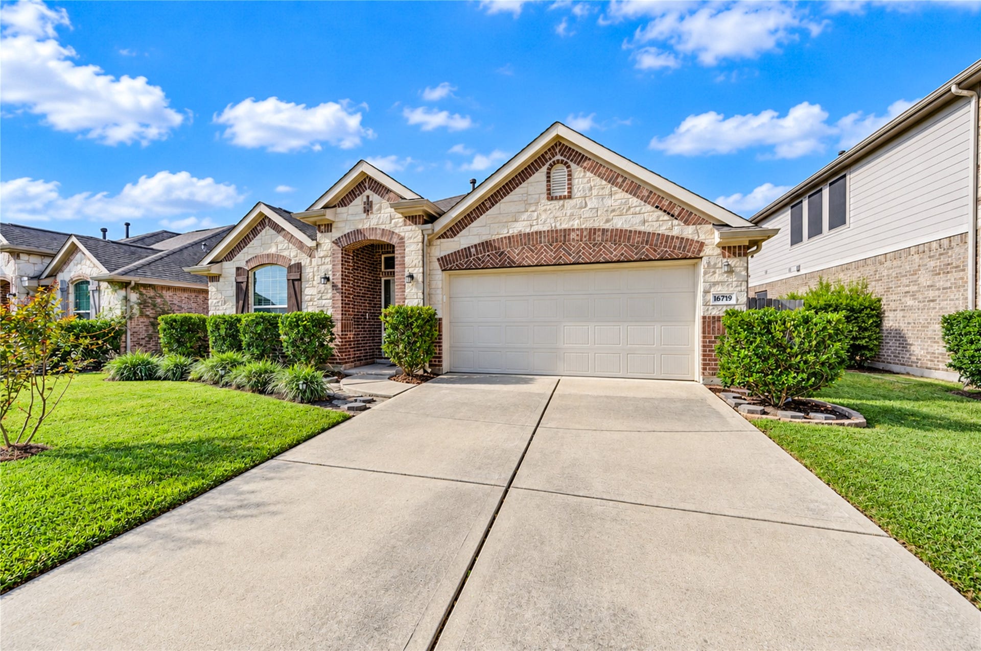 16719 Cactus Blossom Trail, Cypress, TX 77433 A gabled front elevation of stone and brick with an arched entry and a two-car garage, set behind a manicured lawn.