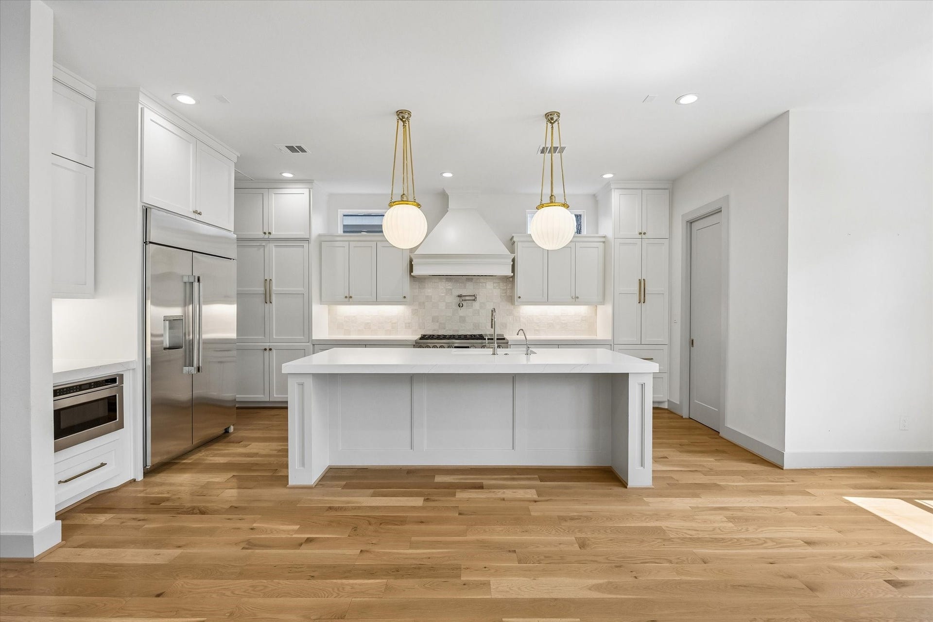 704 Teetshorn Street, Houston, TX 77009 Bright kitchen with white cabinetry, quartz countertops, stainless appliances, brass accents and a large center island.