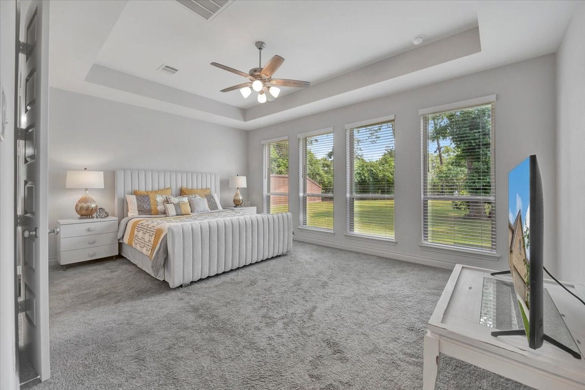 12218 Hickory Arroyo Drive, Humble, TX 77346 Spacious, light-filled bedroom with large windows offering serene views, complemented by a plush carpet and elegant tray ceiling.