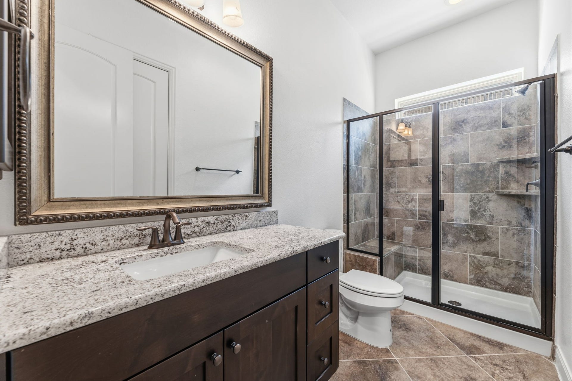 Bathroom featuring a granite countertop with a large, framed mirror and a glass-enclosed shower.