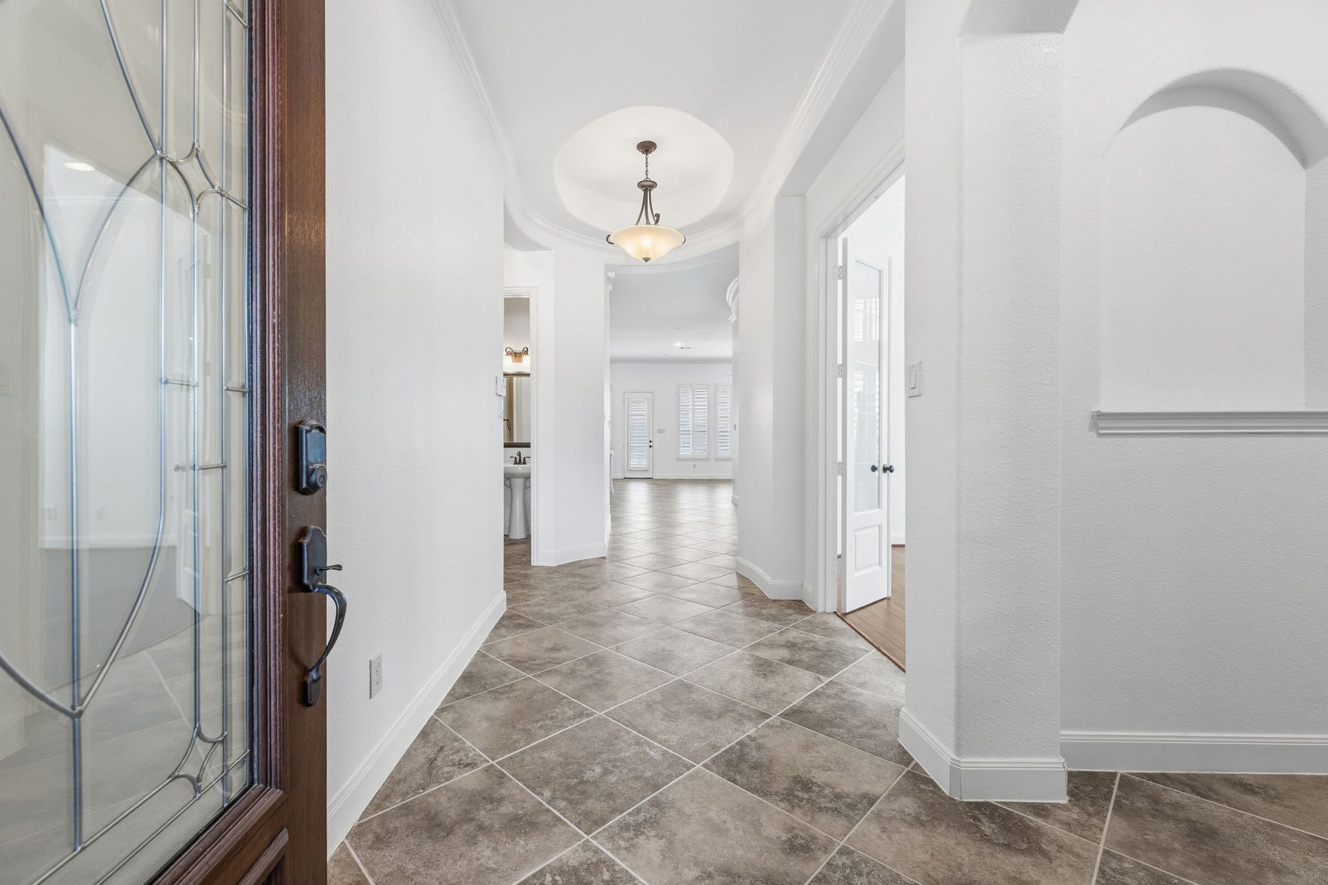 Step into a welcoming entryway featuring tile flooring, a stylish light fixture, and a view into the bright, open living area