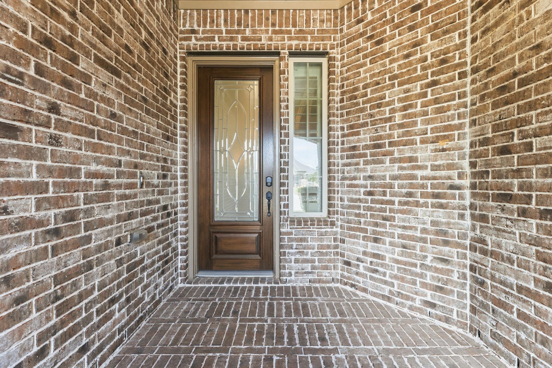Brick front porch with a beautiful wooden door featuring decorative glass panels
