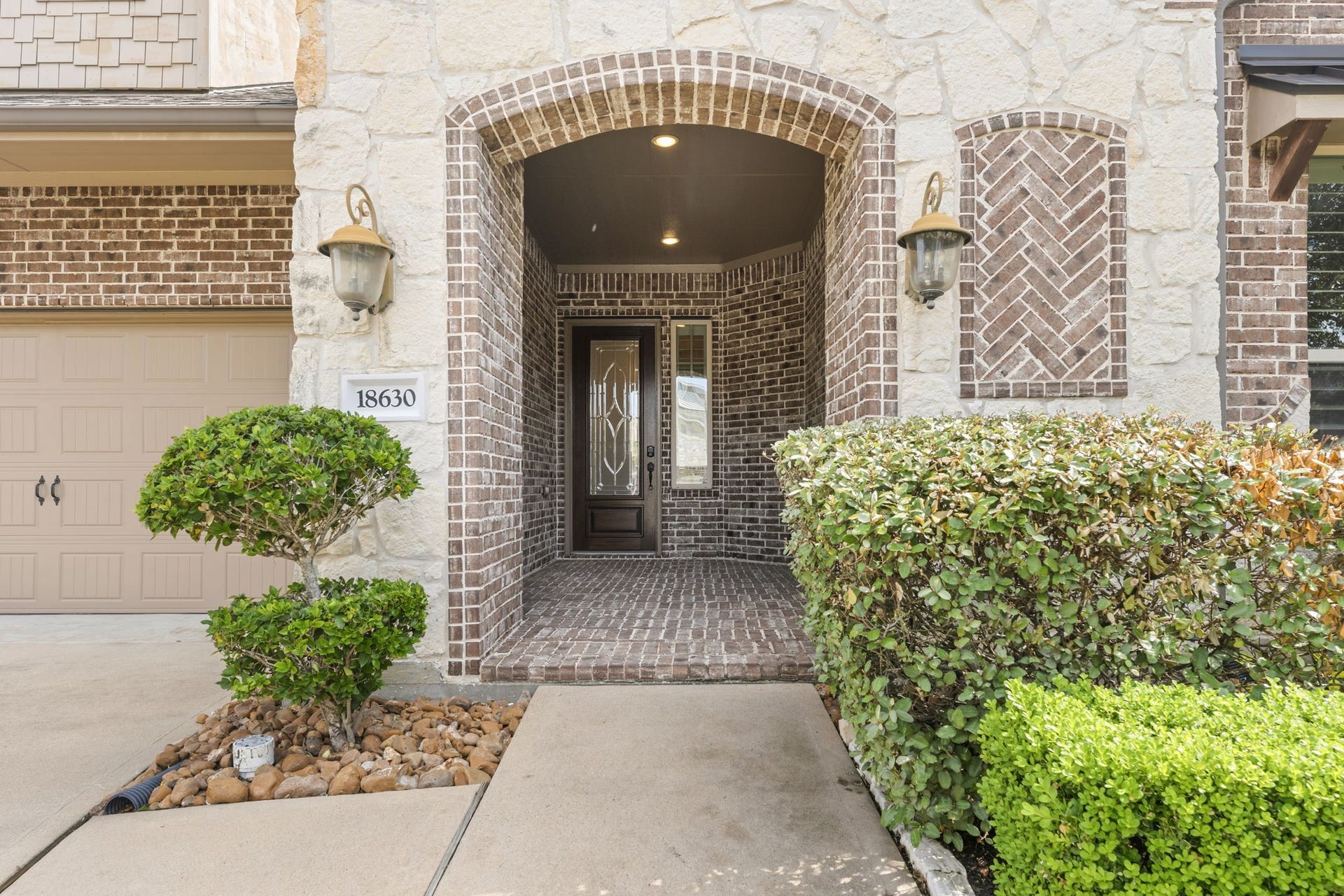 Charming stone and brick entryway with arched design and well-maintained landscaping, creating a welcoming entrance to the home.