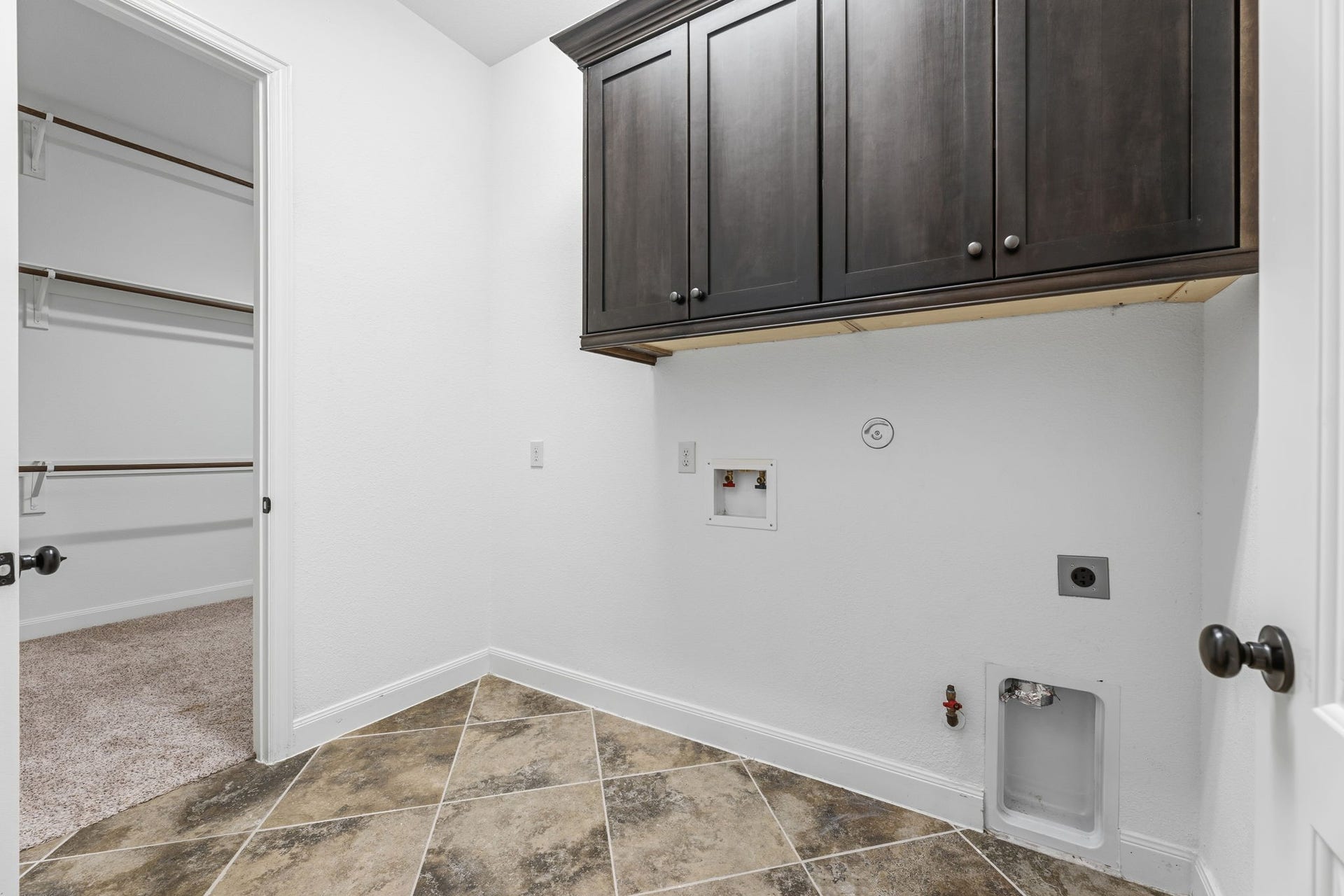 Utility room featurs upper cabinets for extra storage and easy access to the primary closet.
