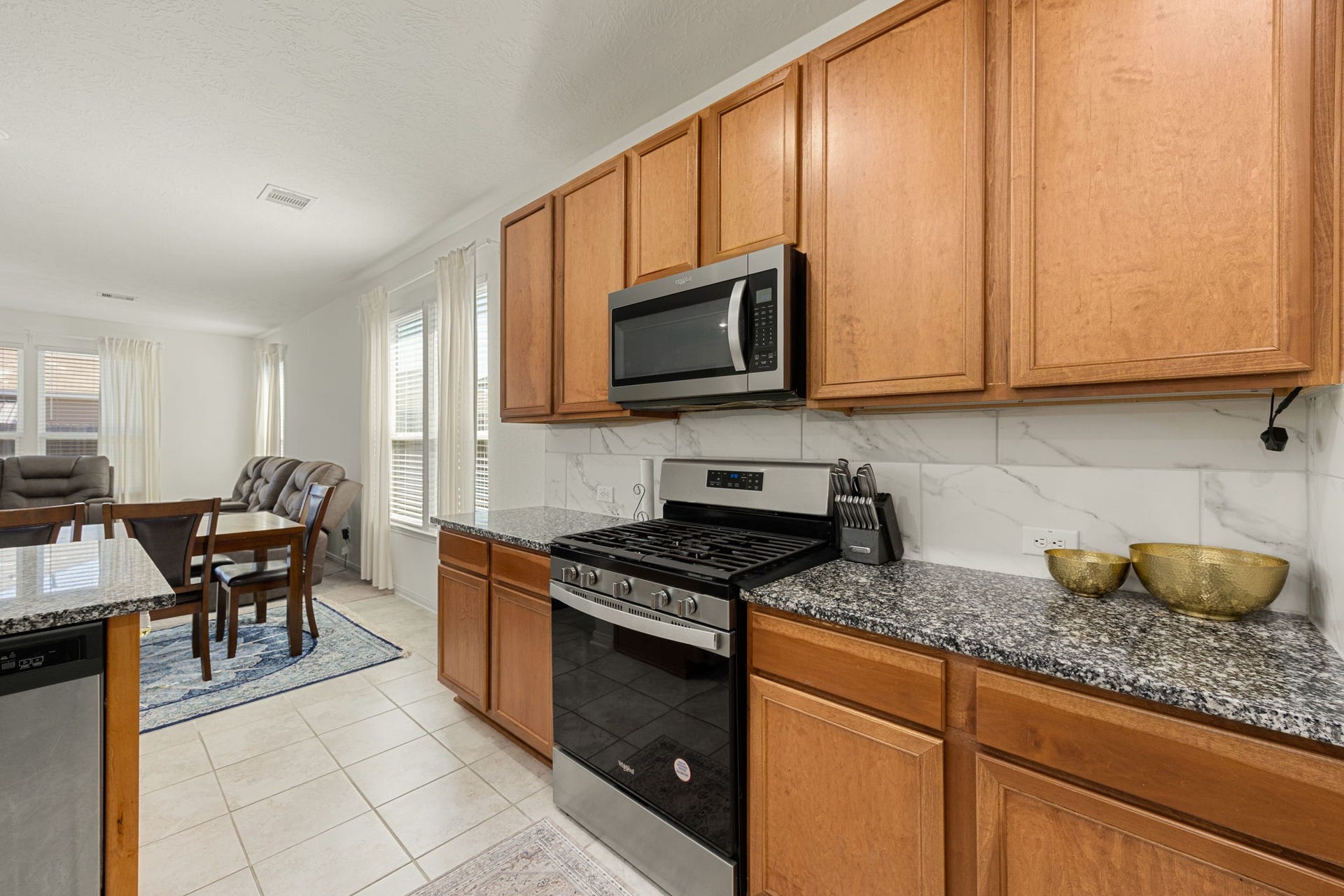 2023 Katalonia Lane, Fresno, TX 77459 The beautifully appointed kitchen showcases a classic balance of warmth and modern design. Premium granite countertops are paired with a timeless marble-patterned tile backsplash, while matching stainless steel Whirlpool appliancesincluding a built-in microwave and gas rangecreate a highly functional workspace for any home chef.