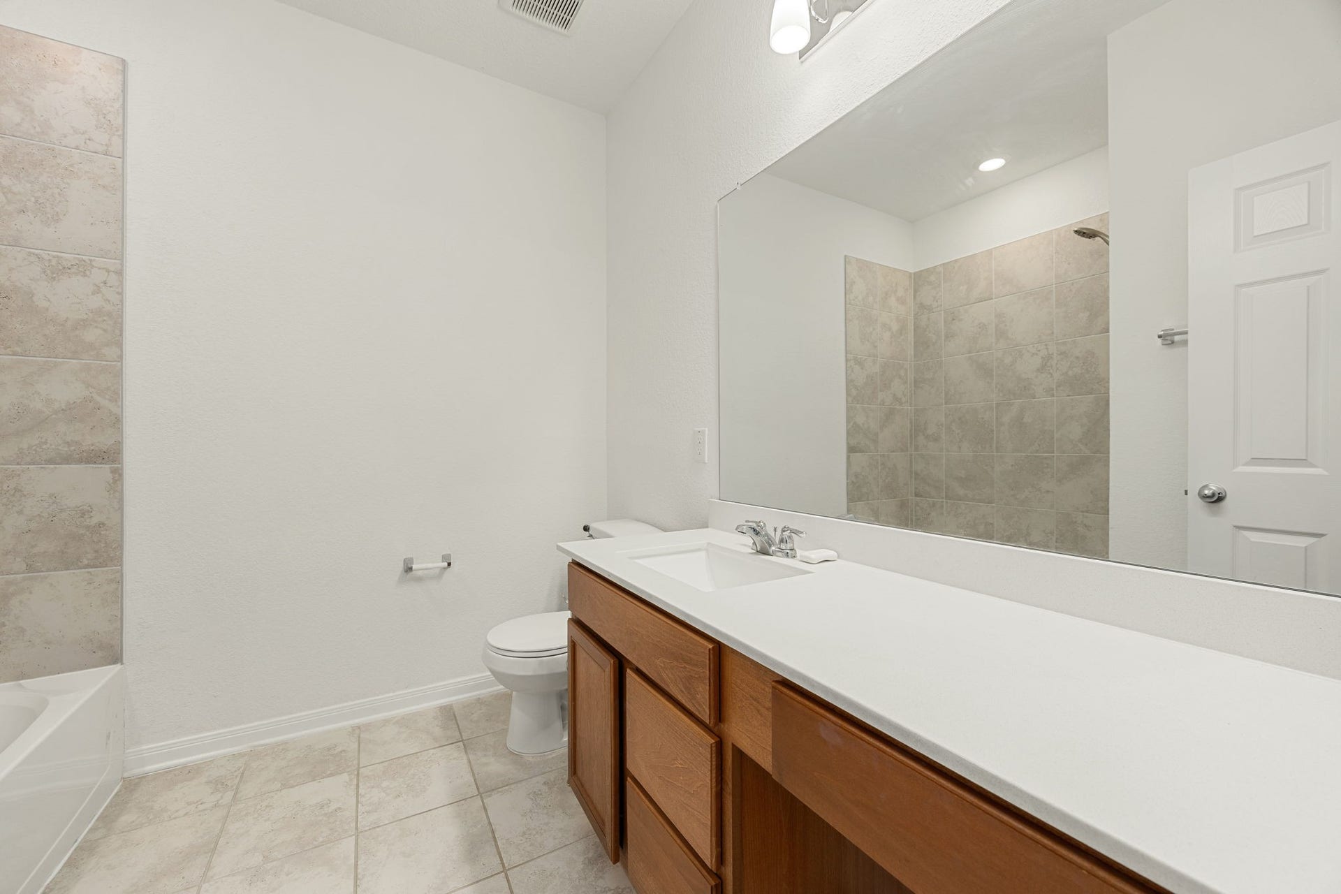 2023 Katalonia Lane, Fresno, TX 77459 The spacious secondary bathroom features an expansive vanity with an integrated sink, an extra-wide mirror, and a convenient sit-down vanity knee space. The space is complete with neutral tile flooring and a clean shower/tub combo wrapped in classic oversized tiling.
