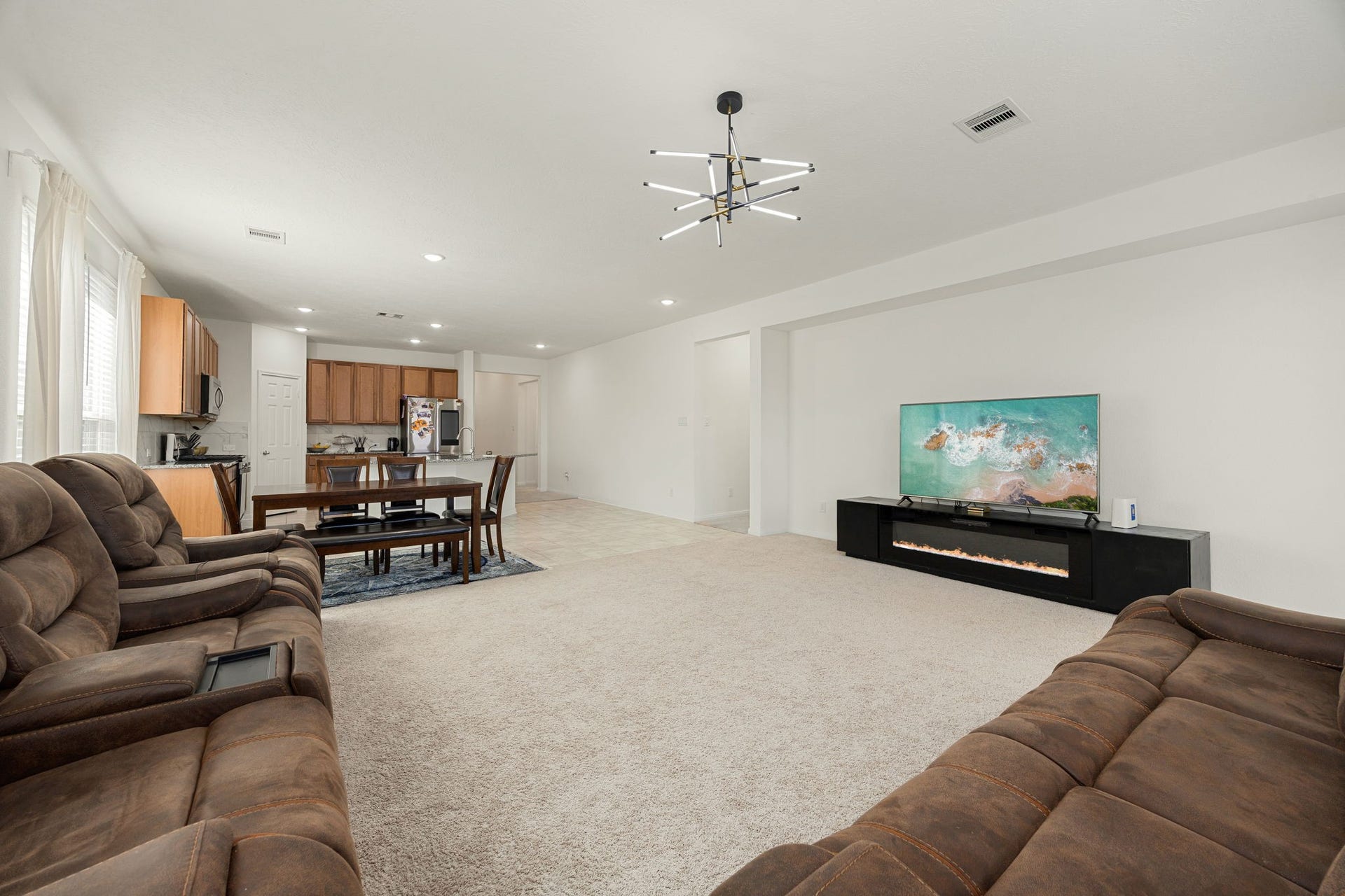 2023 Katalonia Lane, Fresno, TX 77459 Anchoring the main family room is a striking, contemporary sputnik-style chandelier that adds a touch of modern sophistication to the home's high ceilings. This vantage point perfectly showcases the ultimate open-concept layout, demonstrating how smoothly the main seating area flows directly back into the casual dining zone and kitchen hub for cohesive daily living.