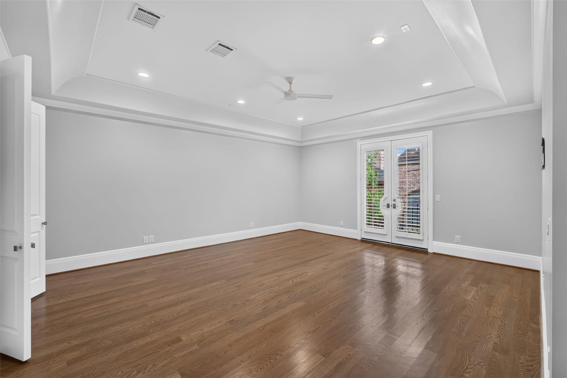 Large primary bedroom with coffered ceilings, balcony and enough space for a sitting area.