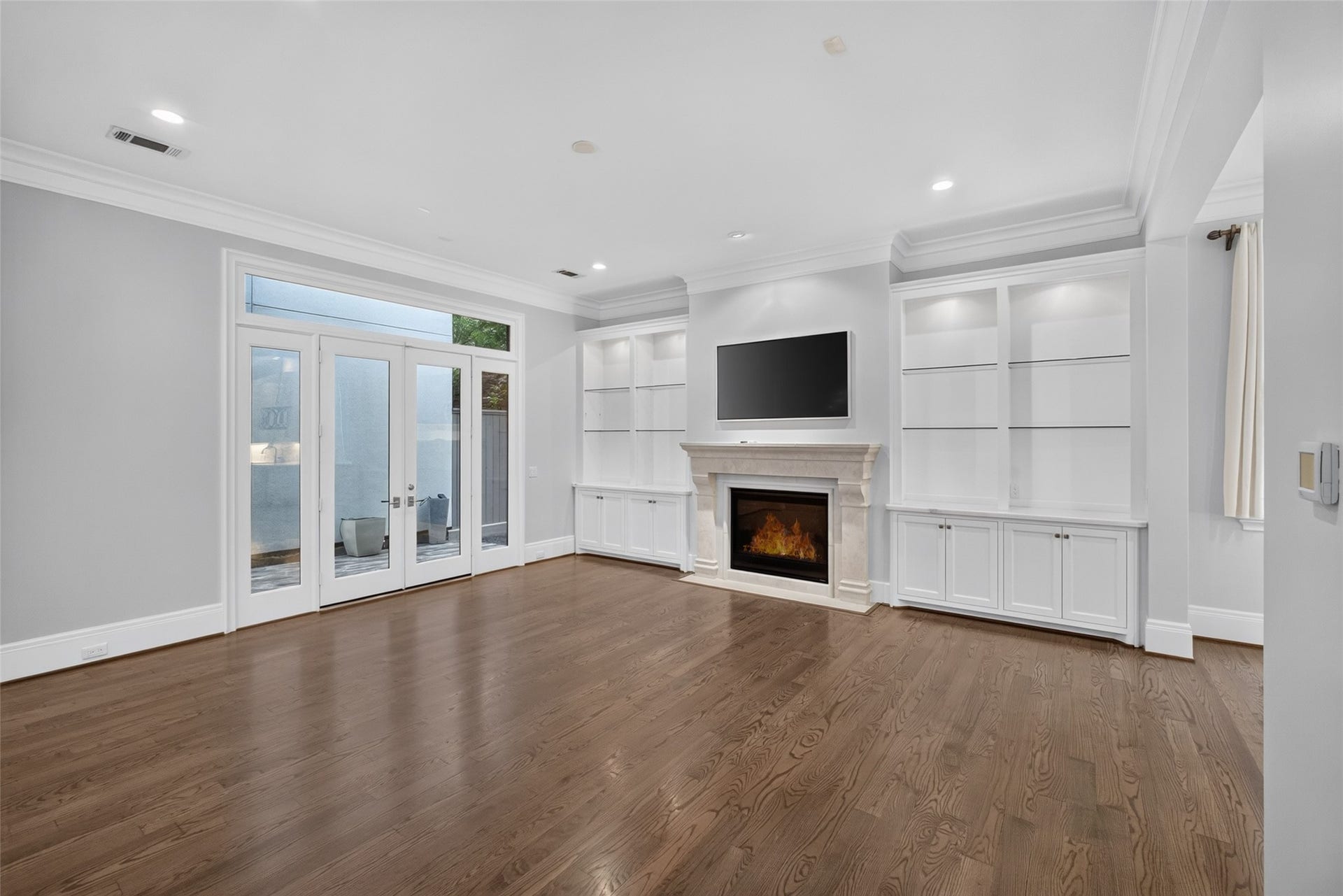 The living room features an elegant stone surround fireplace with a frame TV that conveys with the home. On each side of the fireplace are illuminated glass shelves and storage cabinets.  Notice the large doors to the patio!