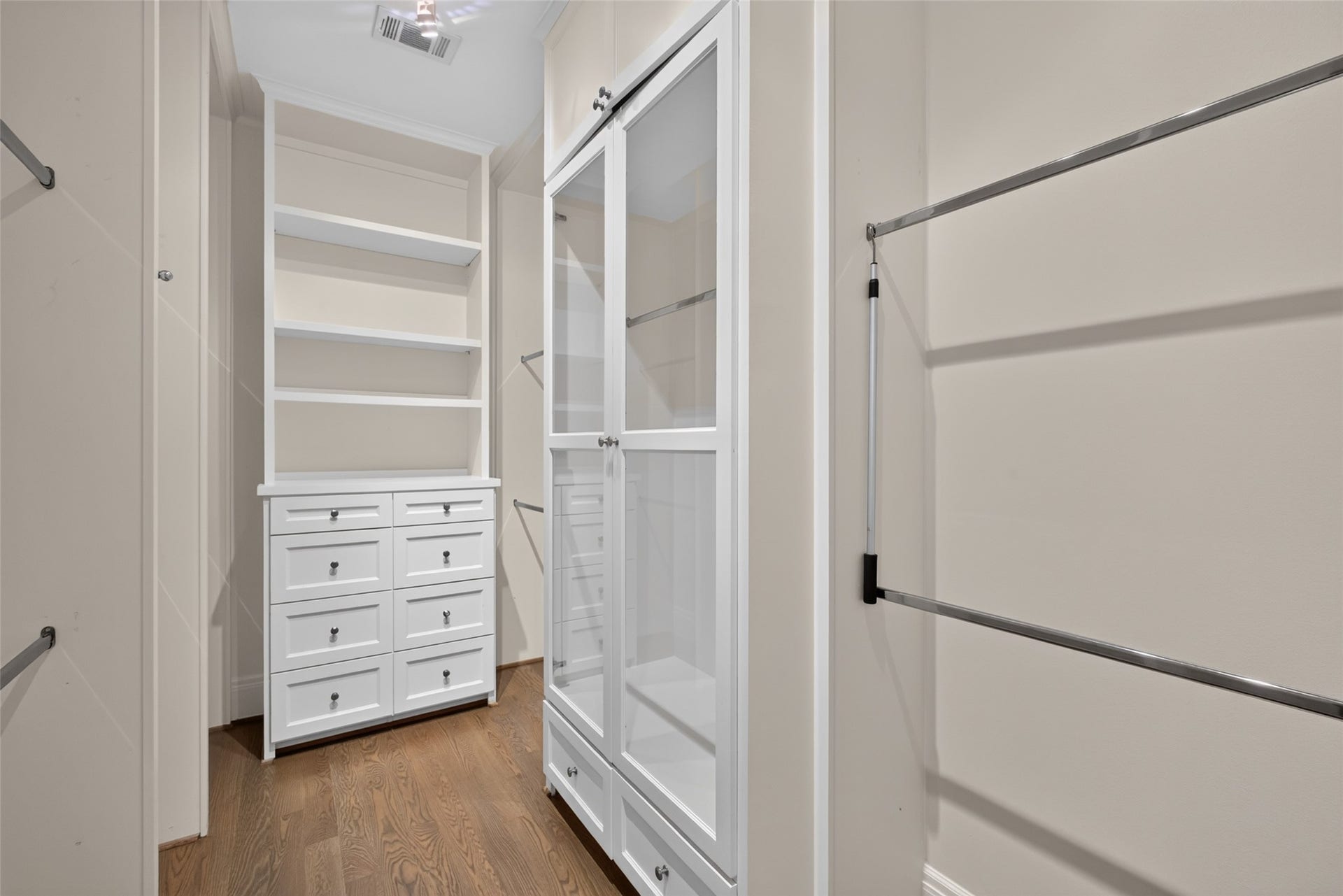 On each side of the shower sit generous walk-in closets.  This one features hanging rods, drawers and shelves.