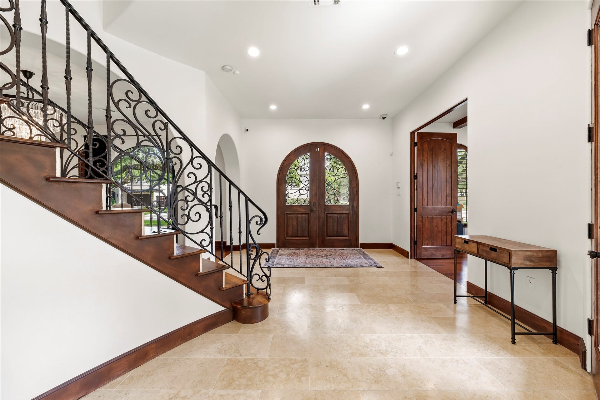 3803 Drake Street, Houston, TX 77005 Stunning arched wood double doors open to a soaring foyer featuring travertine flooring and a custom wrought-iron staircase, setting a tone of timeless luxury from the moment you arrive.