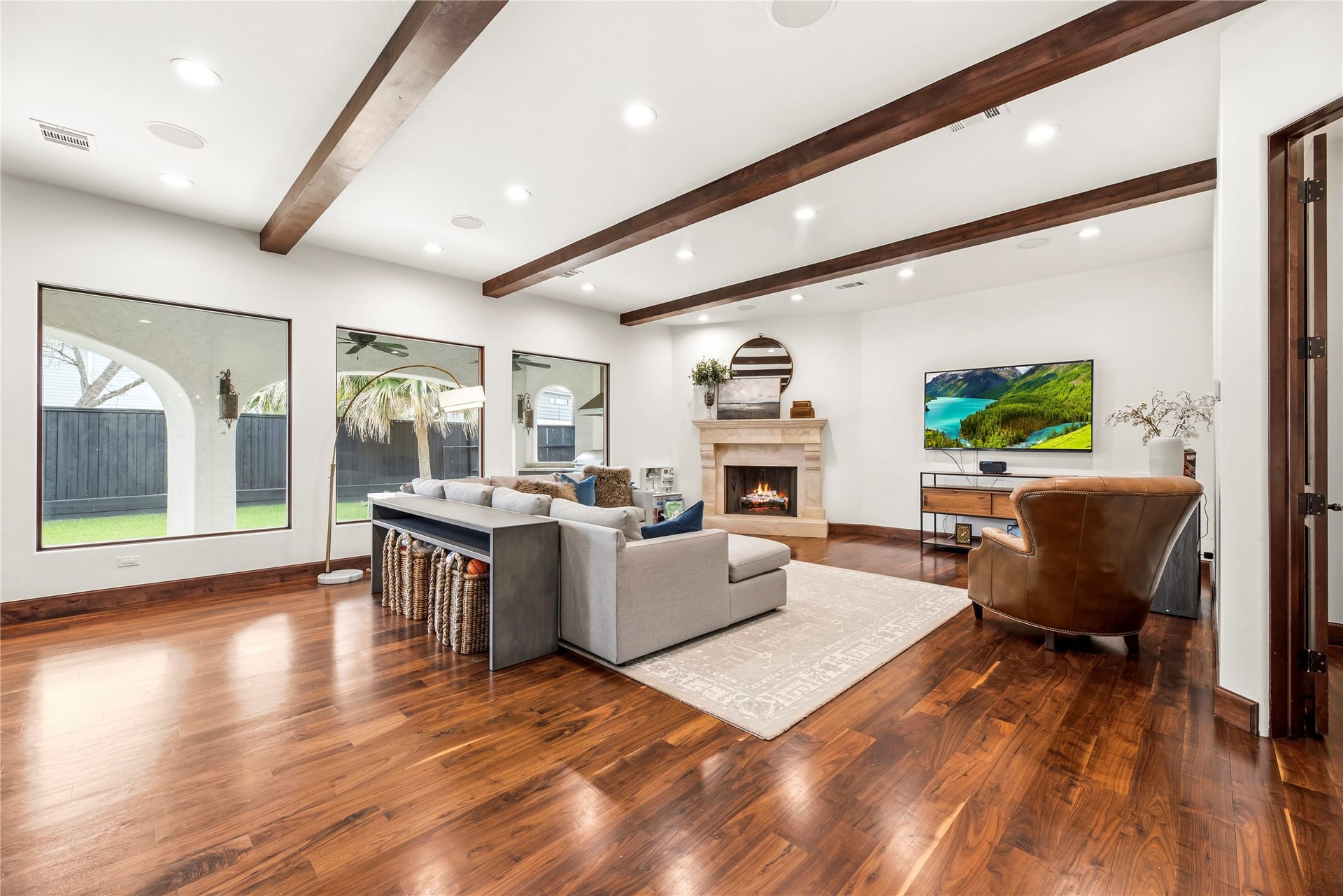 3803 Drake Street, Houston, TX 77005 This luxurious living area is anchored by custom ceiling beams and a stately gas fireplace. Large windows frame peaceful views of the private grounds, creating a sophisticated retreat that blends architectural elegance with a serene outdoor backdrop.