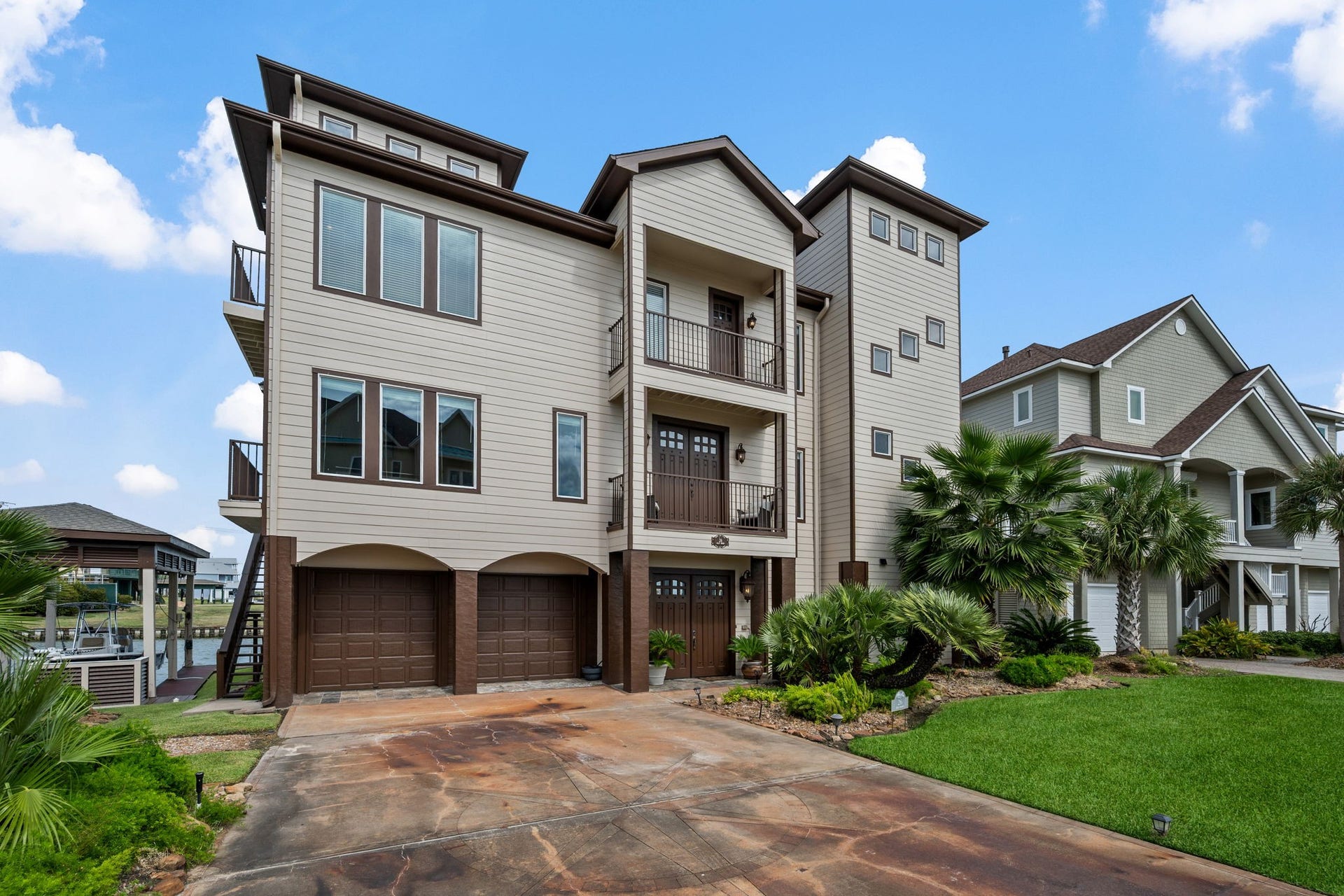 26 Half Moon, Hitchcock, TX 77563 Stunning multi-story coastal home with a modern facade, expansive windows, and lush landscaping, offering ample garage space and a welcoming driveway.