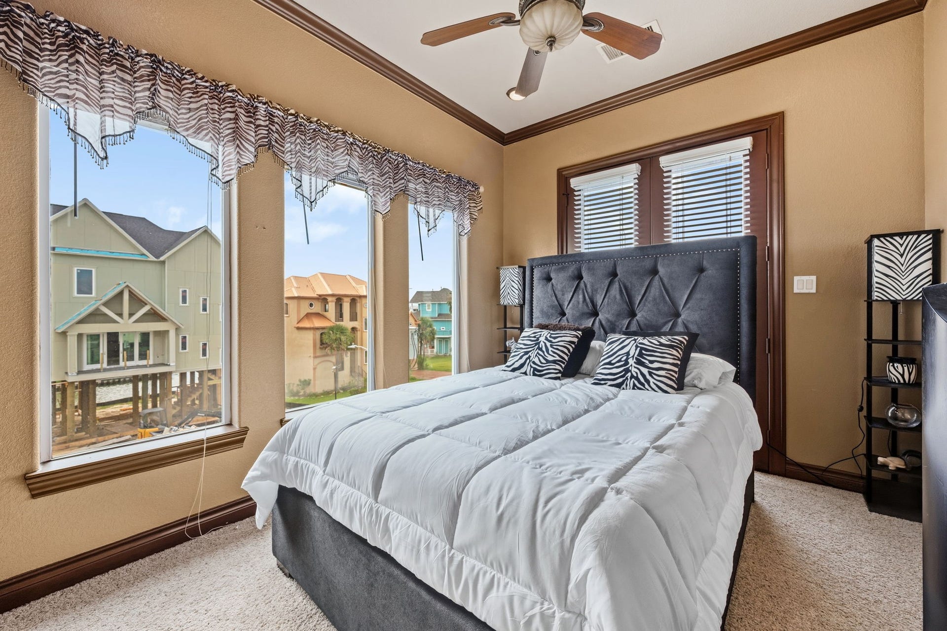 26 Half Moon, Hitchcock, TX 77563 3rd bedroom with large windows offering scenic views, featuring a plush bed with stylish zebra print accents and a ceiling fan for added comfort.