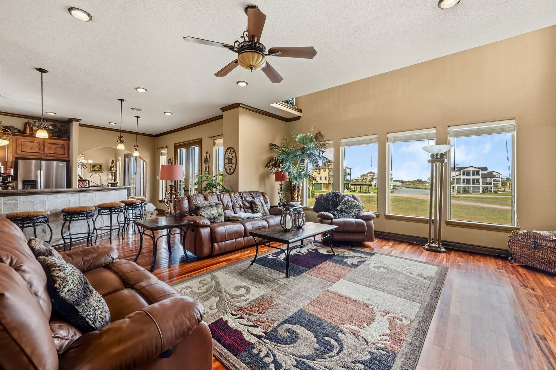 26 Half Moon, Hitchcock, TX 77563 Spacious living area with rich wood flooring and large windows offering scenic views. The open layout seamlessly connects to a modern kitchen with bar seating, creating an inviting space for relaxation and entertaining.