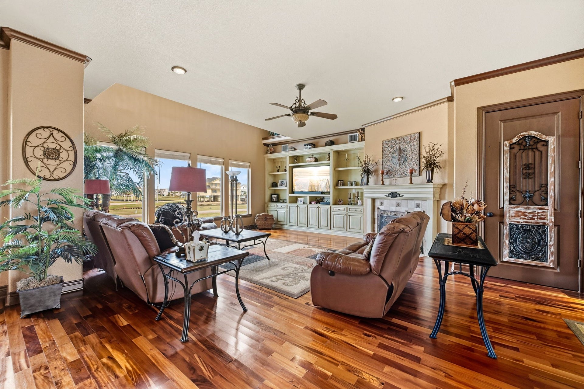 26 Half Moon, Hitchcock, TX 77563 Spacious living room with elegant hardwood floors, cozy leather seating, and a built-in entertainment center. Large windows offer abundant natural light and picturesque views, complemented by tasteful decor and a stylish ceiling fan.