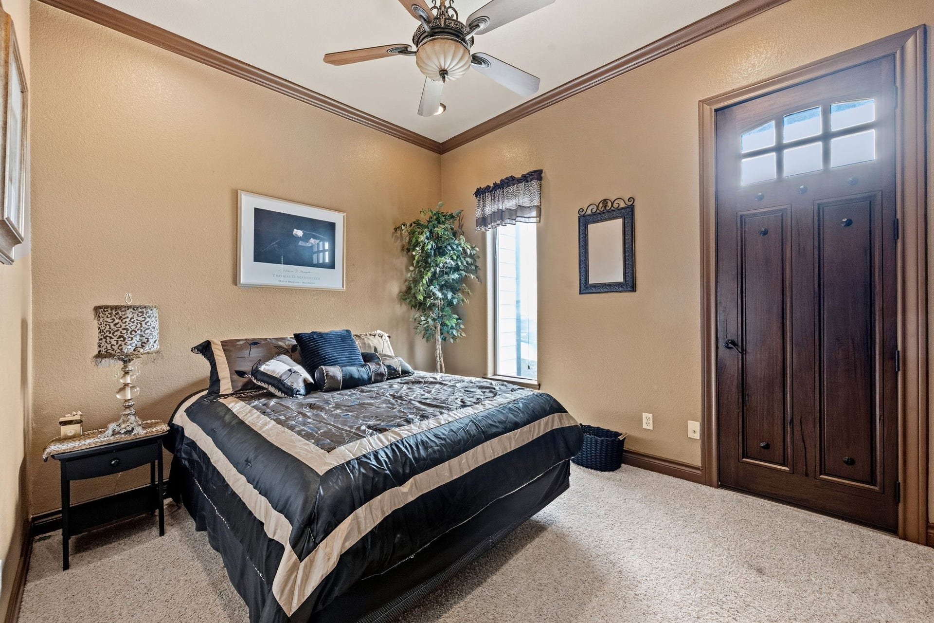 26 Half Moon, Hitchcock, TX 77563 2nd bedroom with warm tones, featuring a ceiling fan, plush carpeting, and a window for natural light. A rich wooden door adds a touch of elegance.