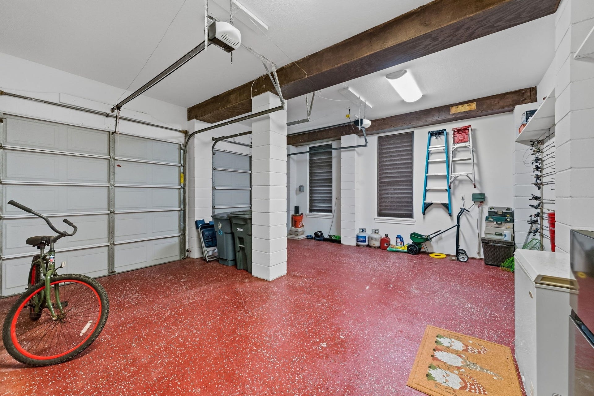 26 Half Moon, Hitchcock, TX 77563 Spacious two-car garage with durable red flooring, ample storage space, and convenient shelving, perfect for organizing tools and outdoor equipment.