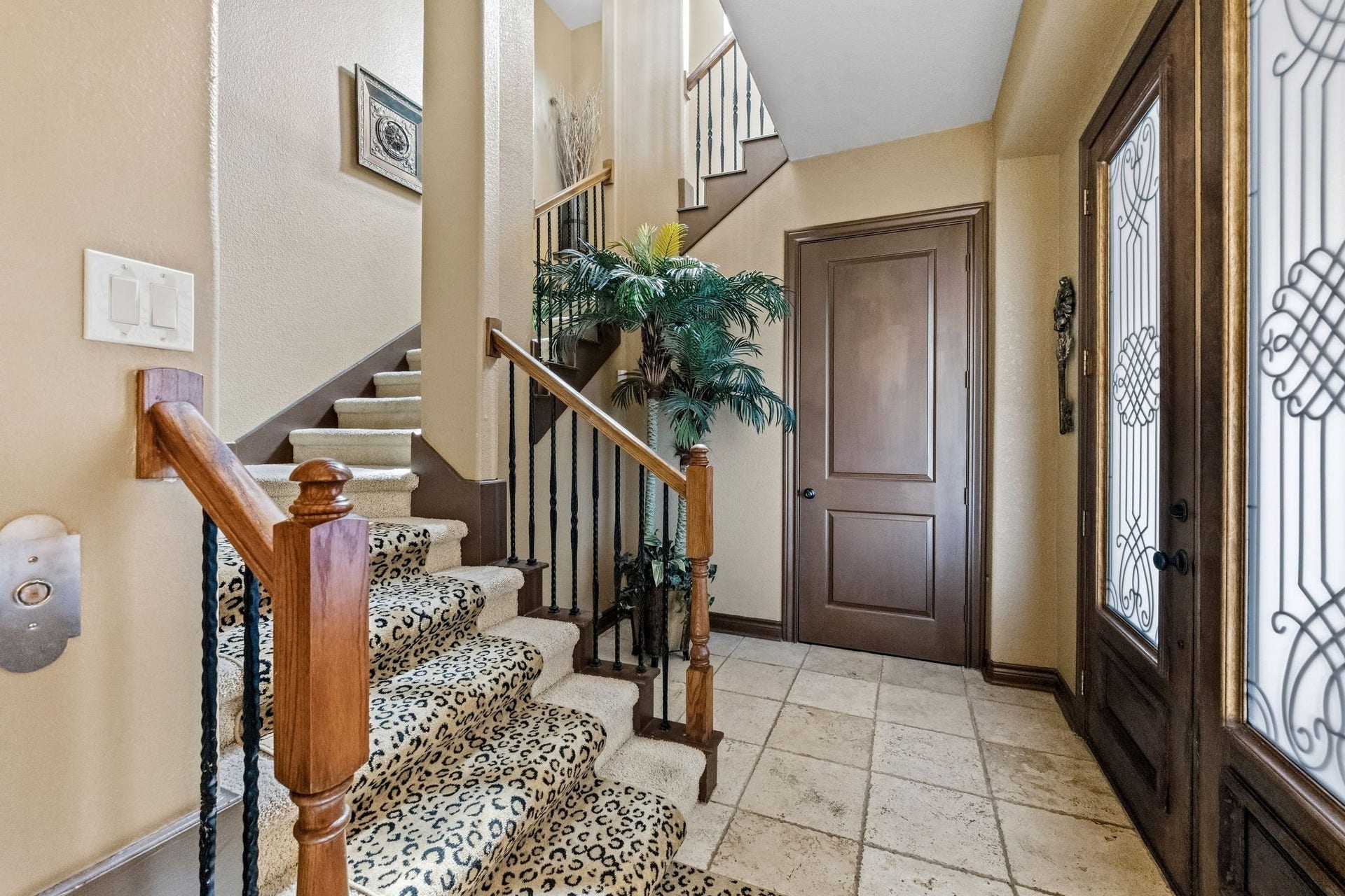 26 Half Moon, Hitchcock, TX 77563 Elegant entryway featuring a carpeted staircase with a bold pattern, intricate ironwork on the doors, and warm wood accents complemented by tile flooring.