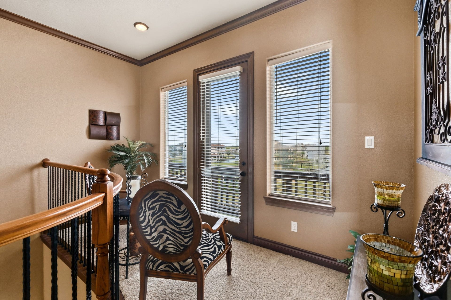26 Half Moon, Hitchcock, TX 77563 Cozy sitting area with abundant natural light, featuring elegant wood accents, a zebra-patterned chair, and access to a balcony with scenic views.
