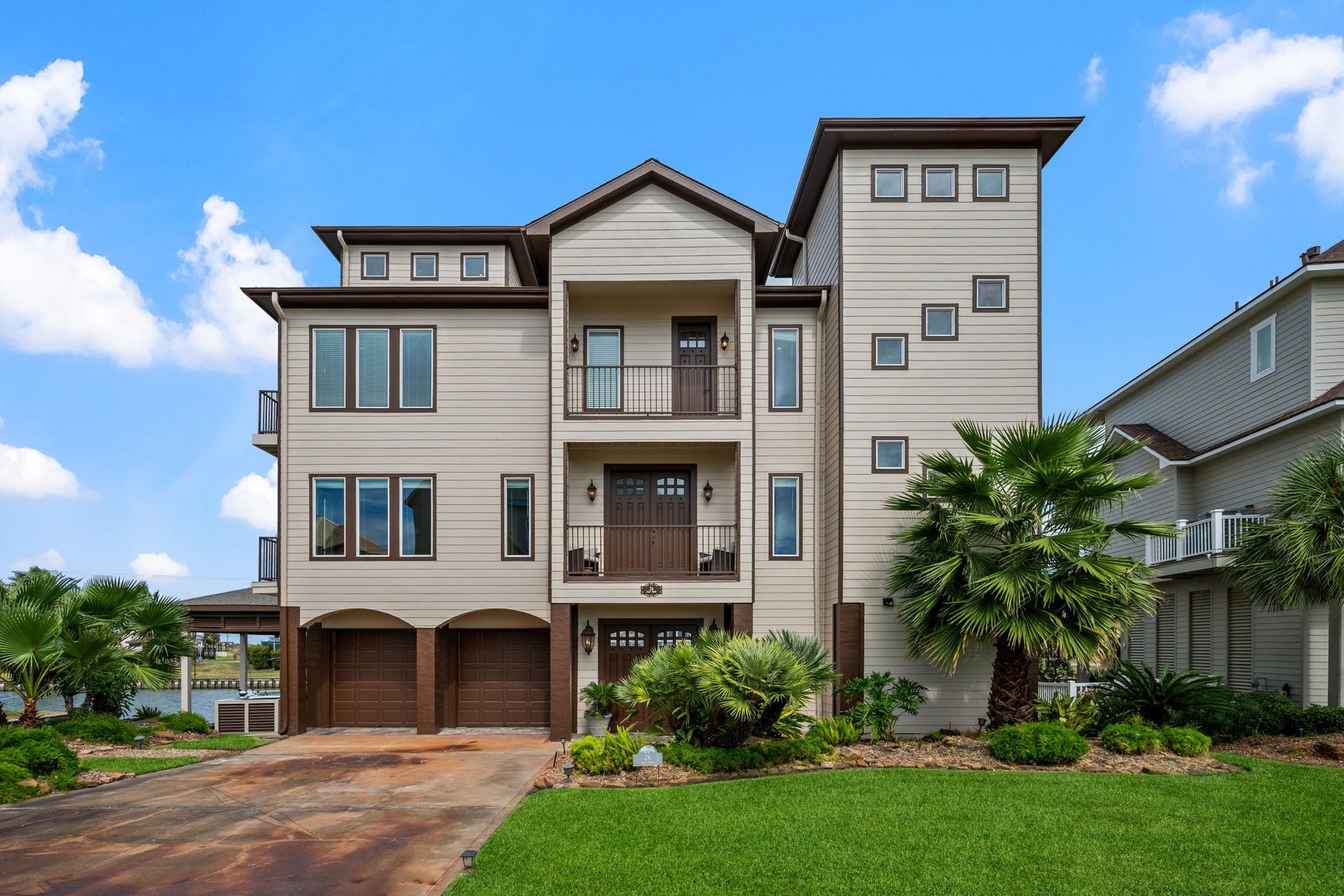 26 Half Moon, Hitchcock, TX 77563 Stunning three-story coastal home with modern architecture, featuring a spacious driveway, lush landscaping, and elegant balconies perfect for enjoying serene views.