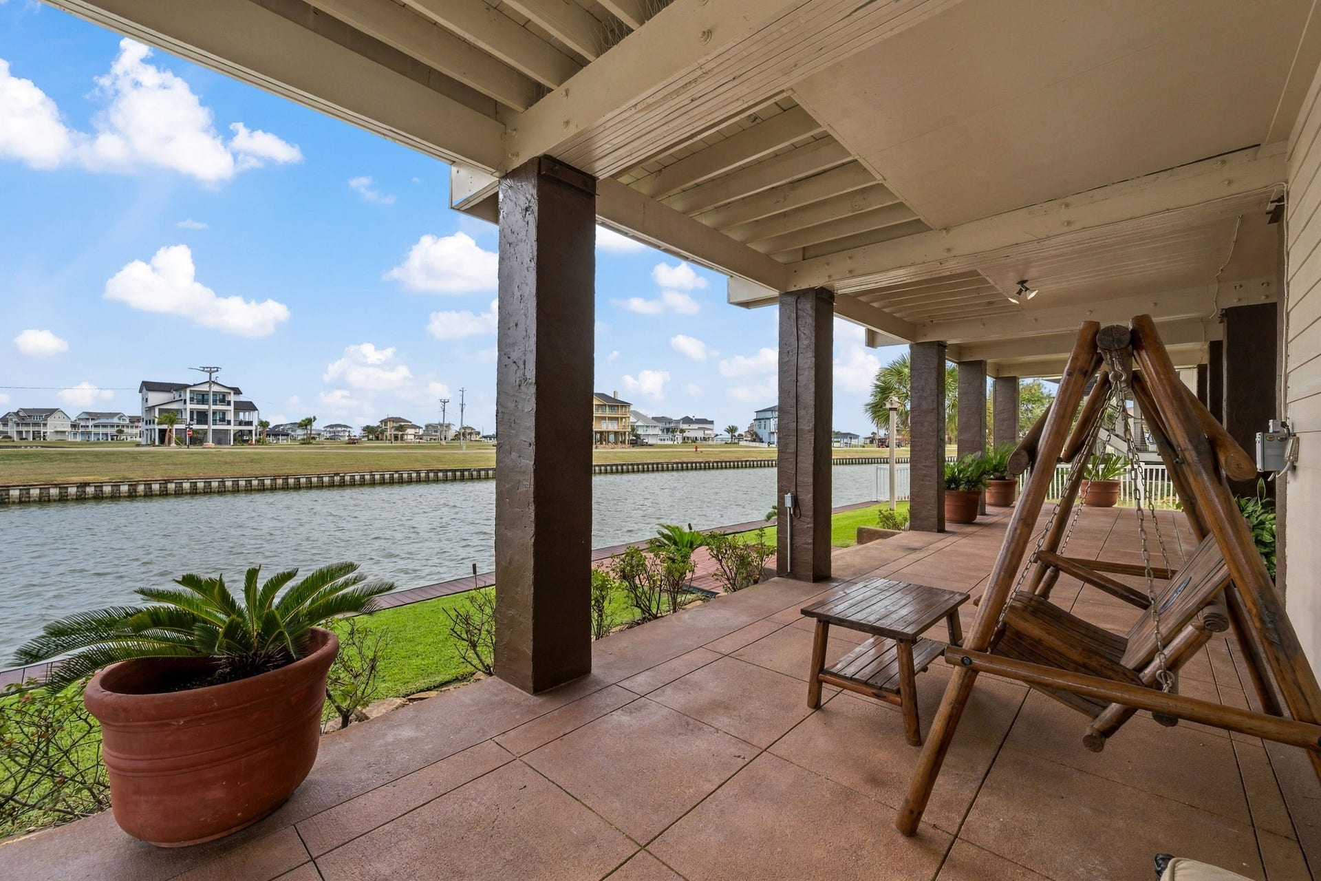 26 Half Moon, Hitchcock, TX 77563 Charming waterfront patio with a cozy wooden swing and serene canal views, perfect for relaxing and enjoying the outdoors.