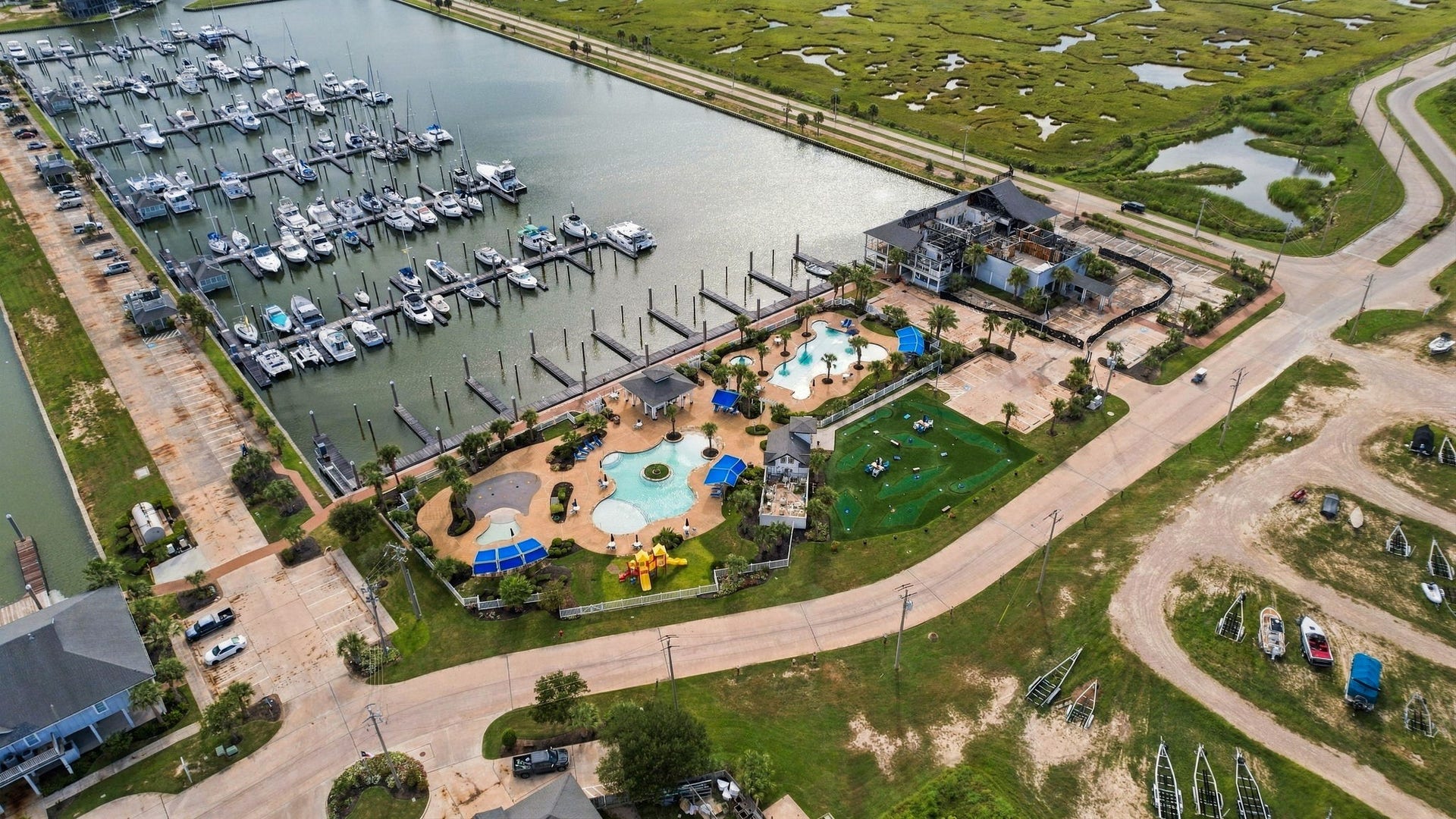 26 Half Moon, Hitchcock, TX 77563 Experience waterfront living with a scenic marina view, featuring well-maintained docks and a vibrant recreational area complete with pools and playgrounds, all nestled within lush greenery.