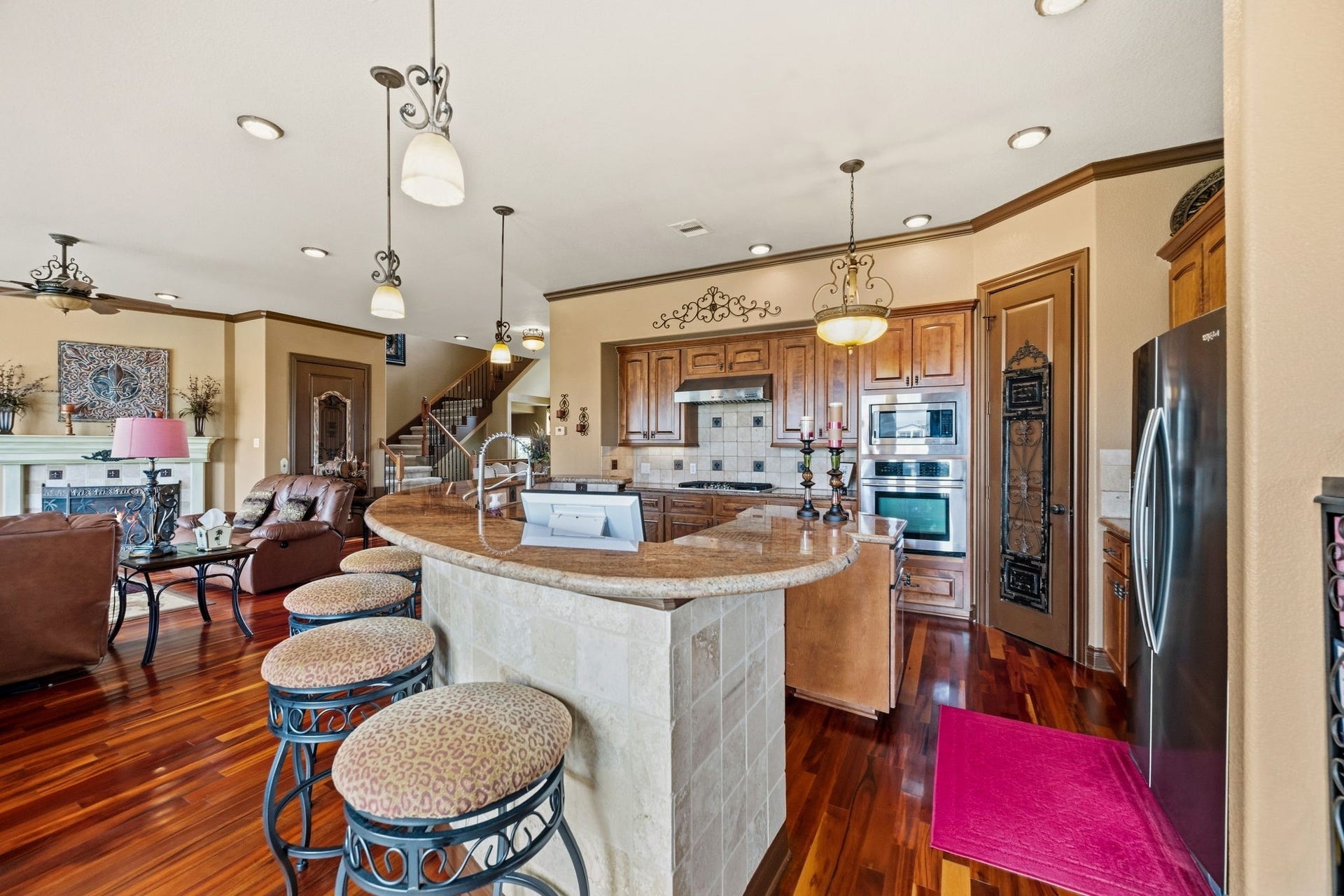 26 Half Moon, Hitchcock, TX 77563 Elegant open-concept kitchen and living area featuring rich hardwood floors, a curved breakfast bar with stylish stools, and custom wood cabinetry.