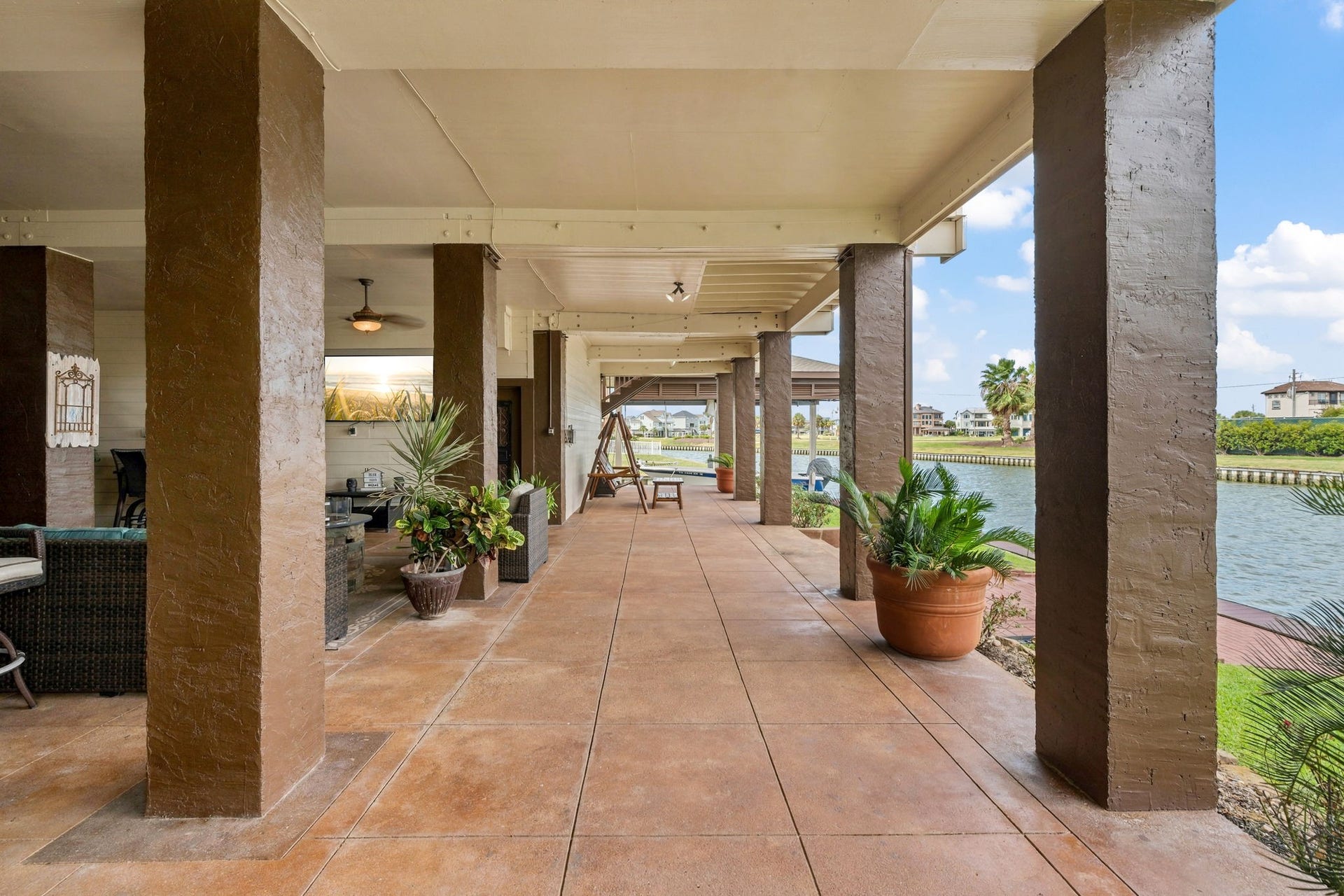 26 Half Moon, Hitchcock, TX 77563 Expansive covered patio with elegant columns and lush potted plants, offering stunning waterfront views and ample space for outdoor relaxation and entertainment.