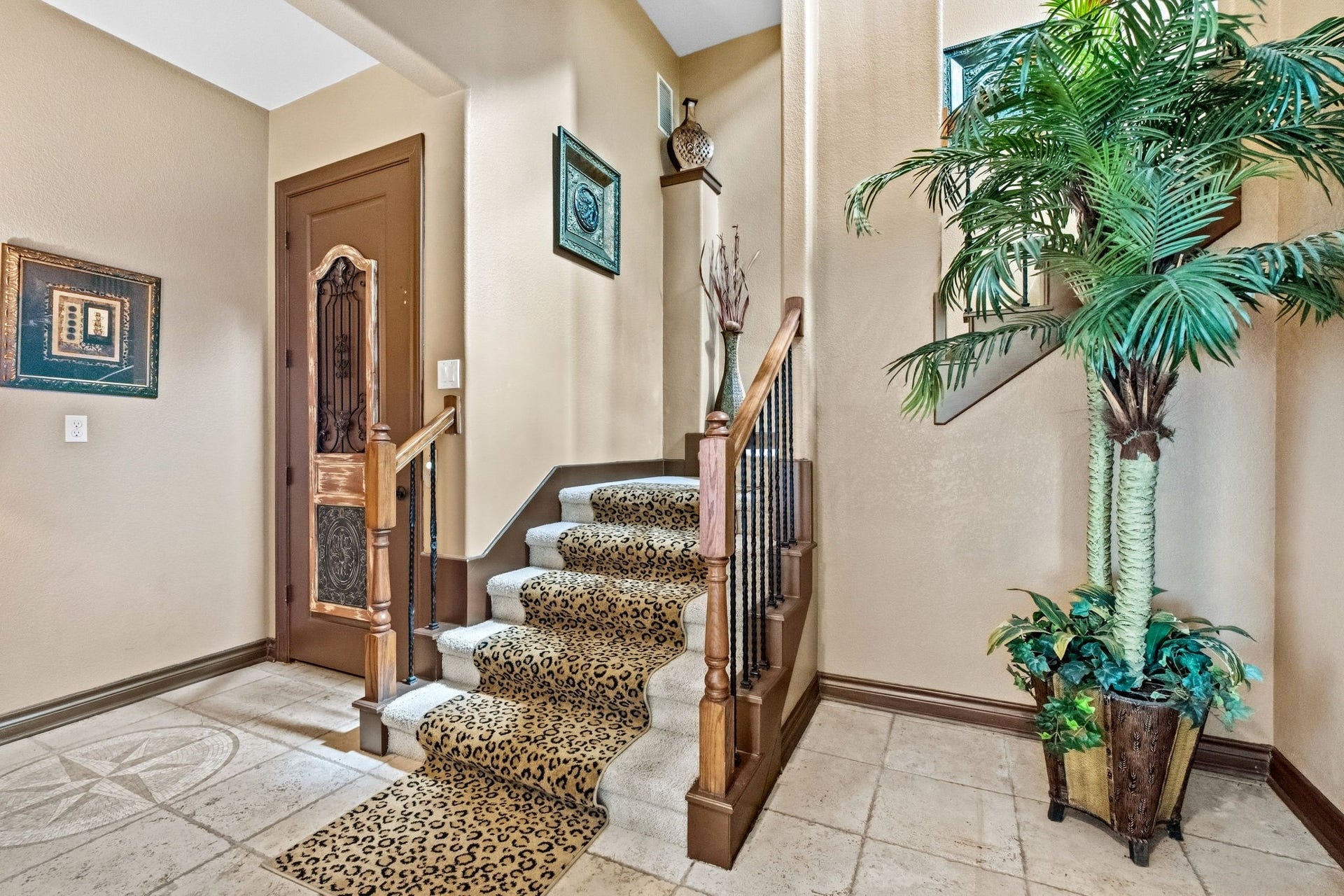 26 Half Moon, Hitchcock, TX 77563 Elegant staircase with ornate wooden railing and leopard-print carpet, complemented by decorative wall art and a lush potted plant, creating a welcoming entrance.